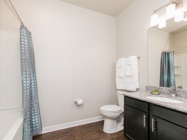 Modern bathroom with a toilet, granite vanity, shower curtain, and towel rack under bright lighting at Apartments at Charlestown Crossing.