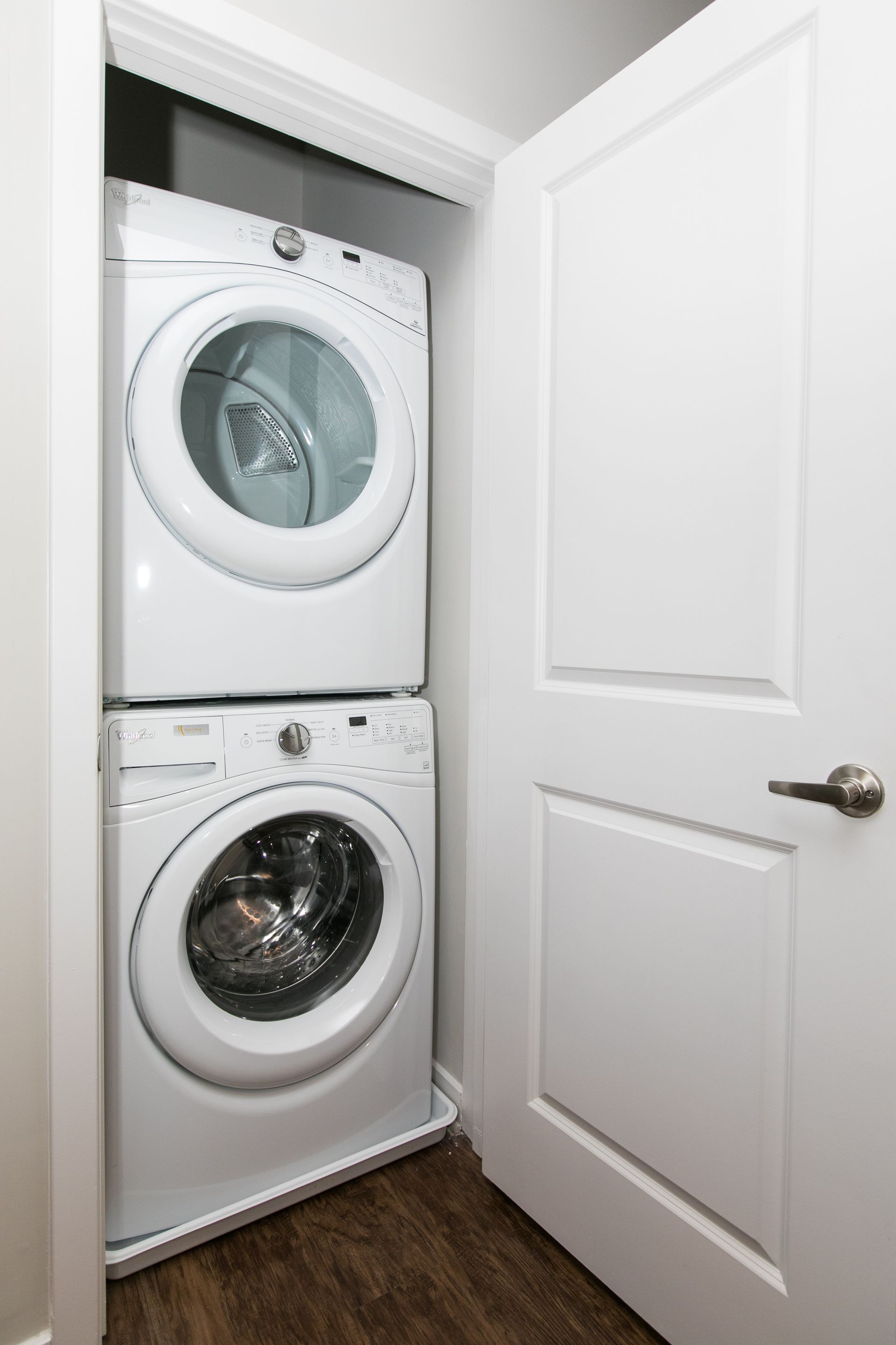 Stacked washer and dryer in a small closet behind a partially open white door at Apartments at Charlestown Crossing.