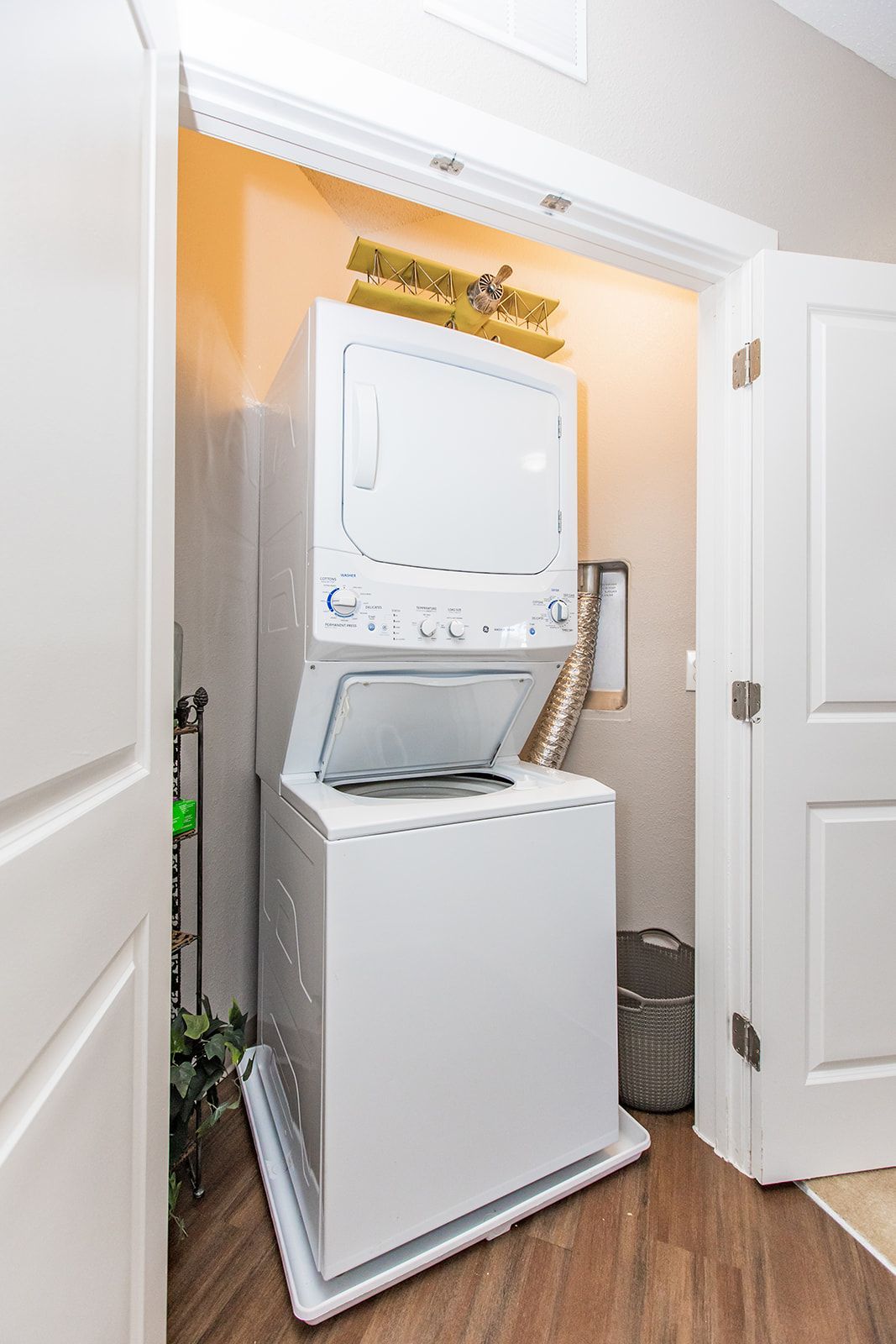 Stacked washer and dryer in a small closet, with the dryer door open and laundry basket nearby at Apartments at Charlestown Crossing.