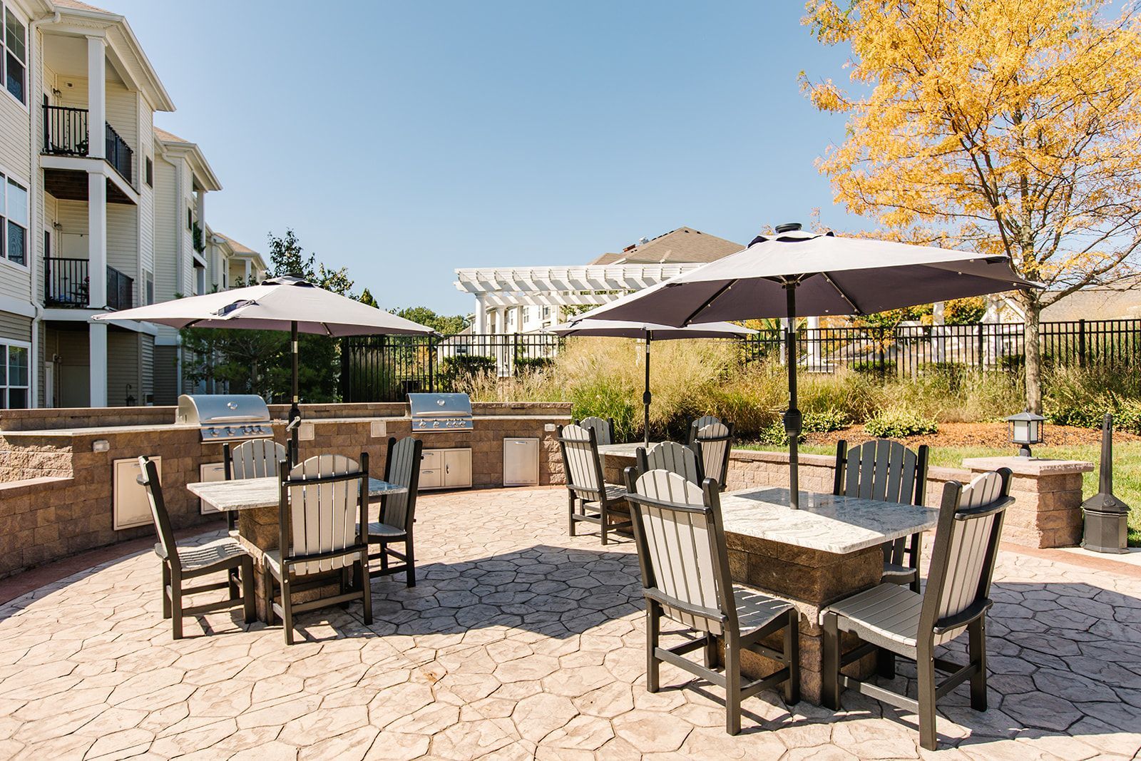 Apartment courtyard patio with tables, chairs, umbrellas, and stone paving under sunny skies at Apartments at Charlestown Crossing.