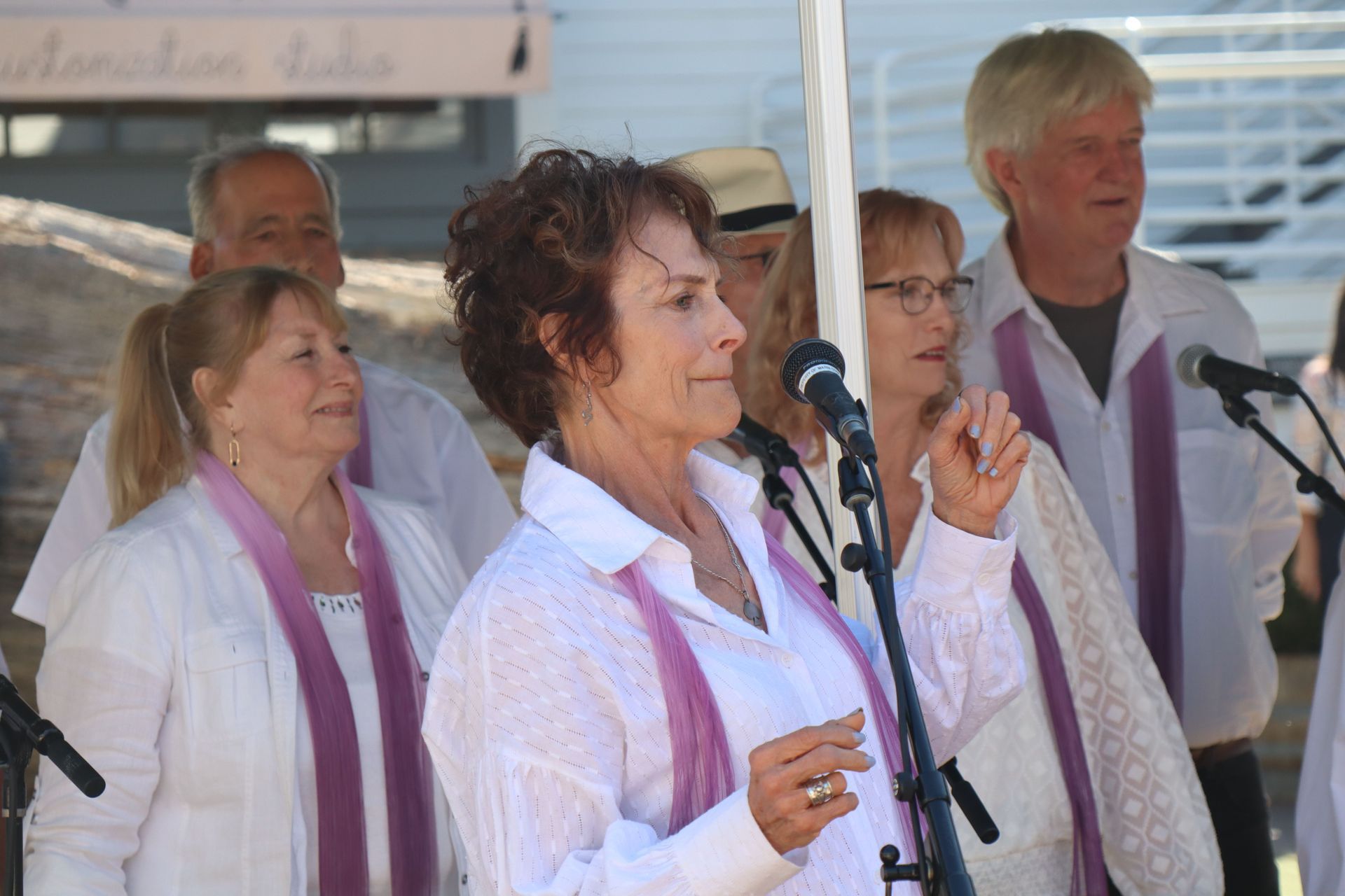 People in white shirts and purple scarves singing at microphones during an outdoor event