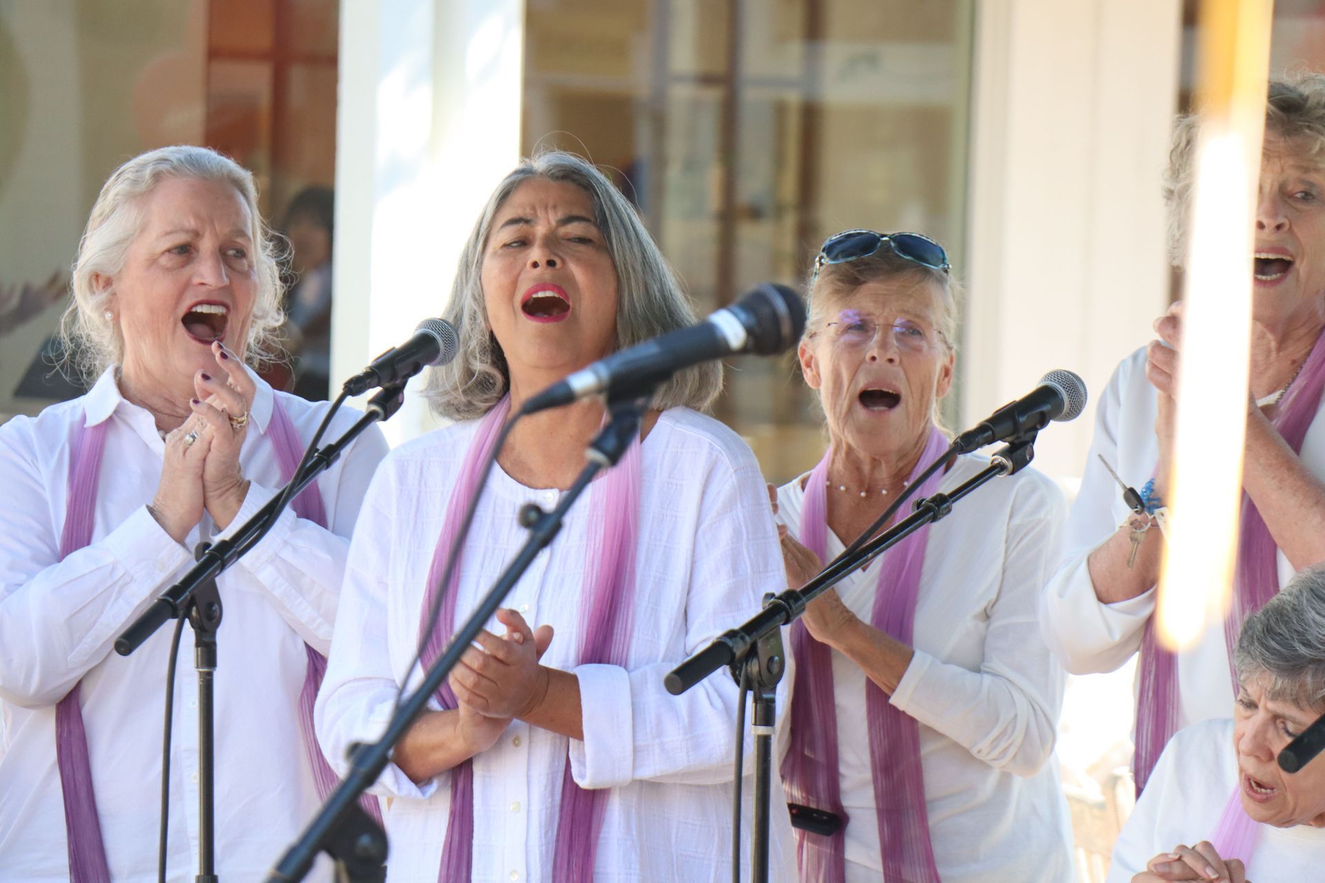 Three singers in white robes performing with microphones at a choir event