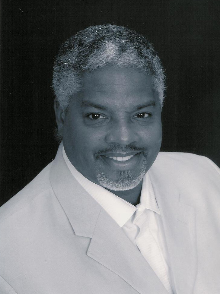 Smiling man in a light suit and tie against a dark background.