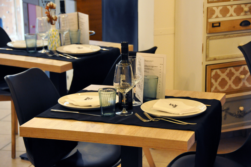 Tavoli da ristorante apparecchiati con piatti, bottiglie e tovaglioli in una sala da pranzo calda e moderna.
