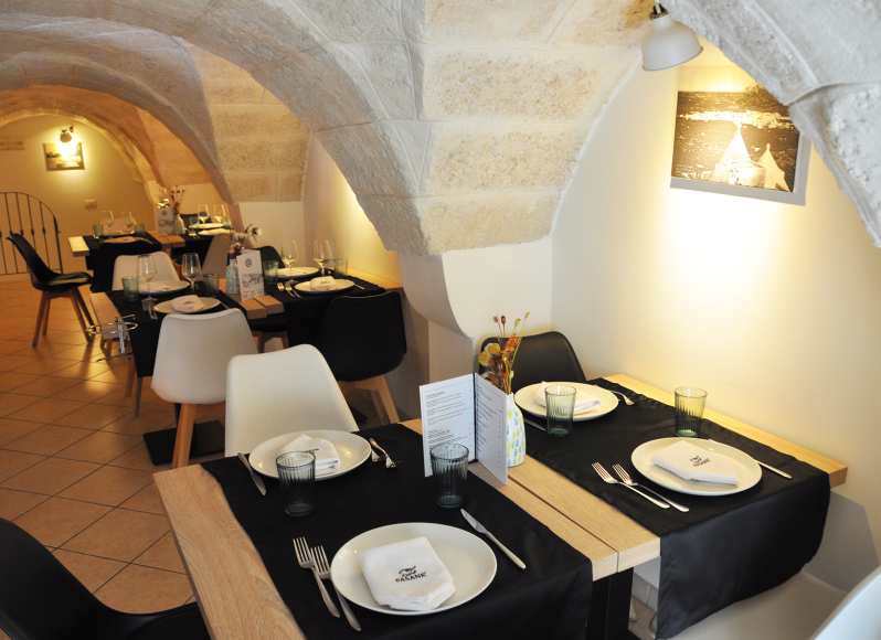 Elegante sala da pranzo ad arco con tovaglie nere, piatti bianchi e luci calde.