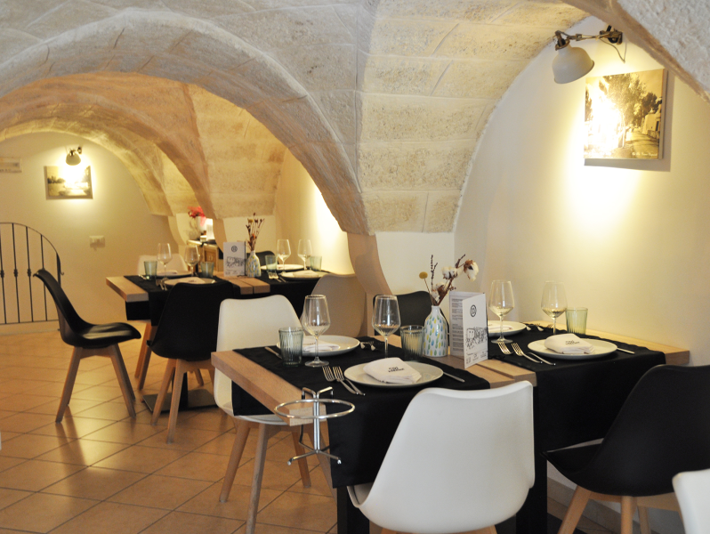 Accogliente interno del ristorante con soffitti a volta in pietra, tavoli apparecchiati e sedie in bianco e nero.