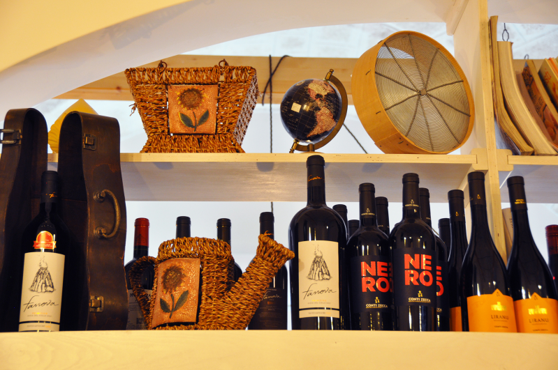 Bottiglie di vino e cesti decorativi disposti su scaffali in una vetrina illuminata da una luce calda.