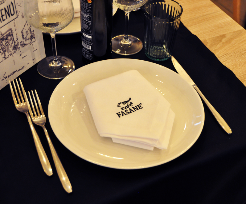 Elegante apparecchiatura da ristorante con piatto bianco, tovagliolo piegato, posate e bicchieri da vino su una tovaglia nera.