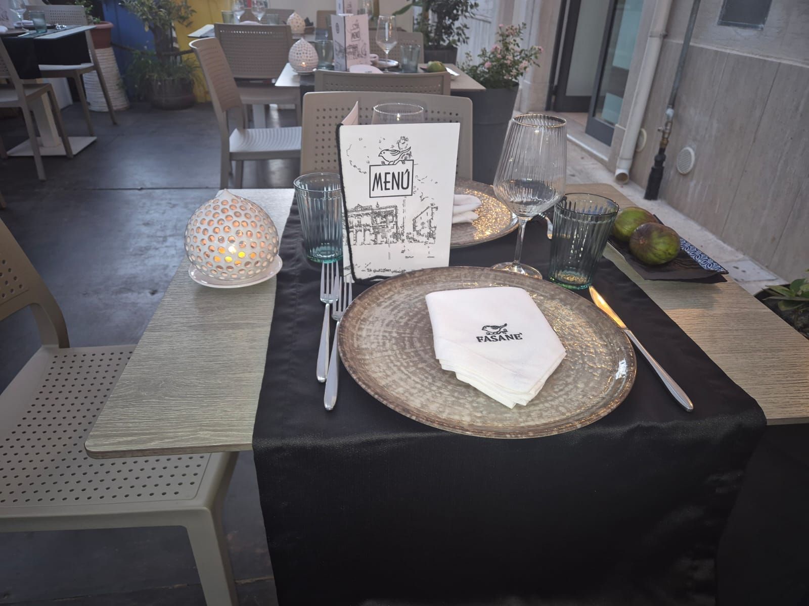 Tavolo da pranzo decorato con menù, tovaglioli, piatti e centrotavola con candele in un ambiente da ristorante.