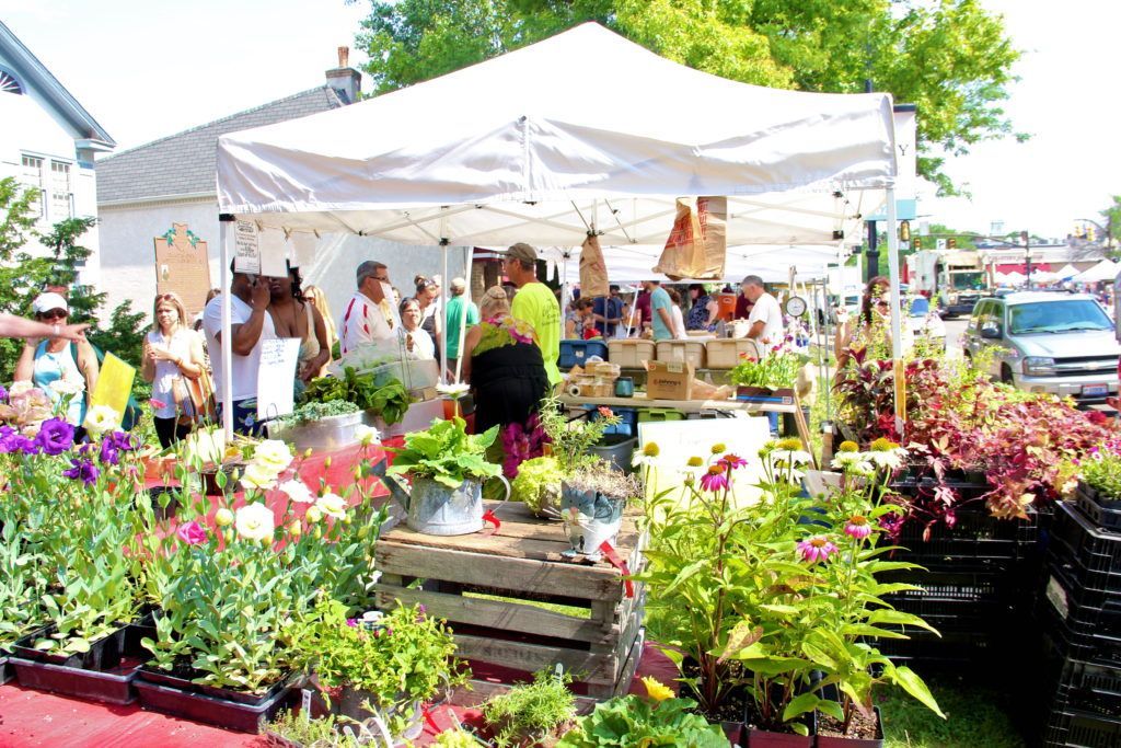 A group of people are standing under a white tent at a flower market.