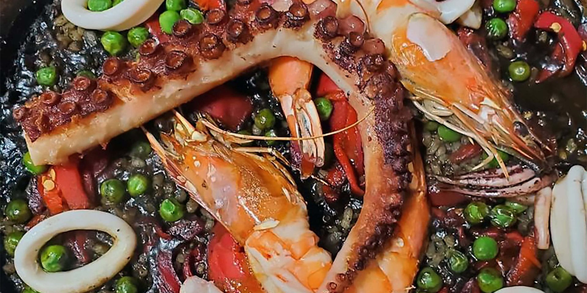 A close up of a plate of food with shrimp , octopus , squid and peas.