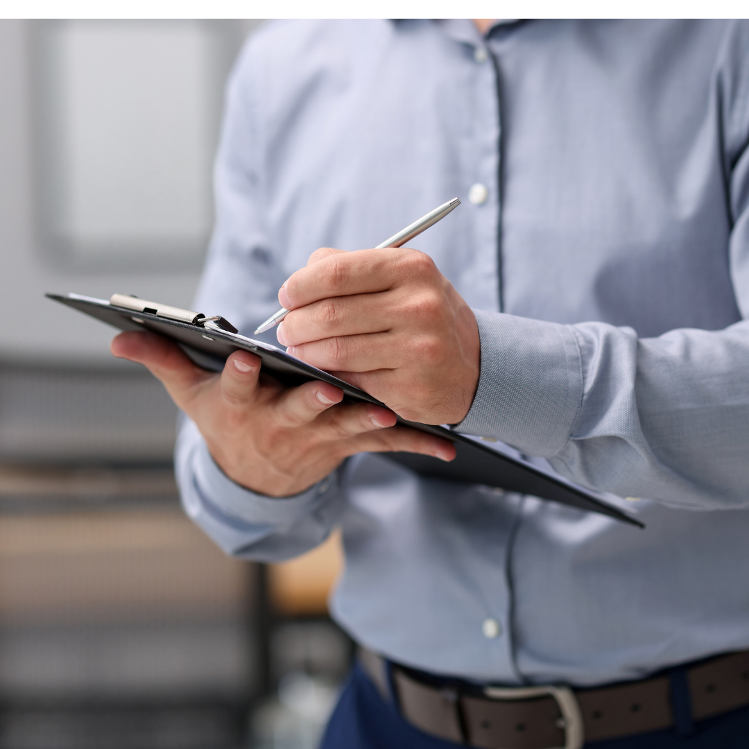 Person in a light blue shirt writing on a clipboard with a pen in an office setting