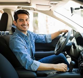 Man smiling while driving a car. He is wearing a denim shirt.
