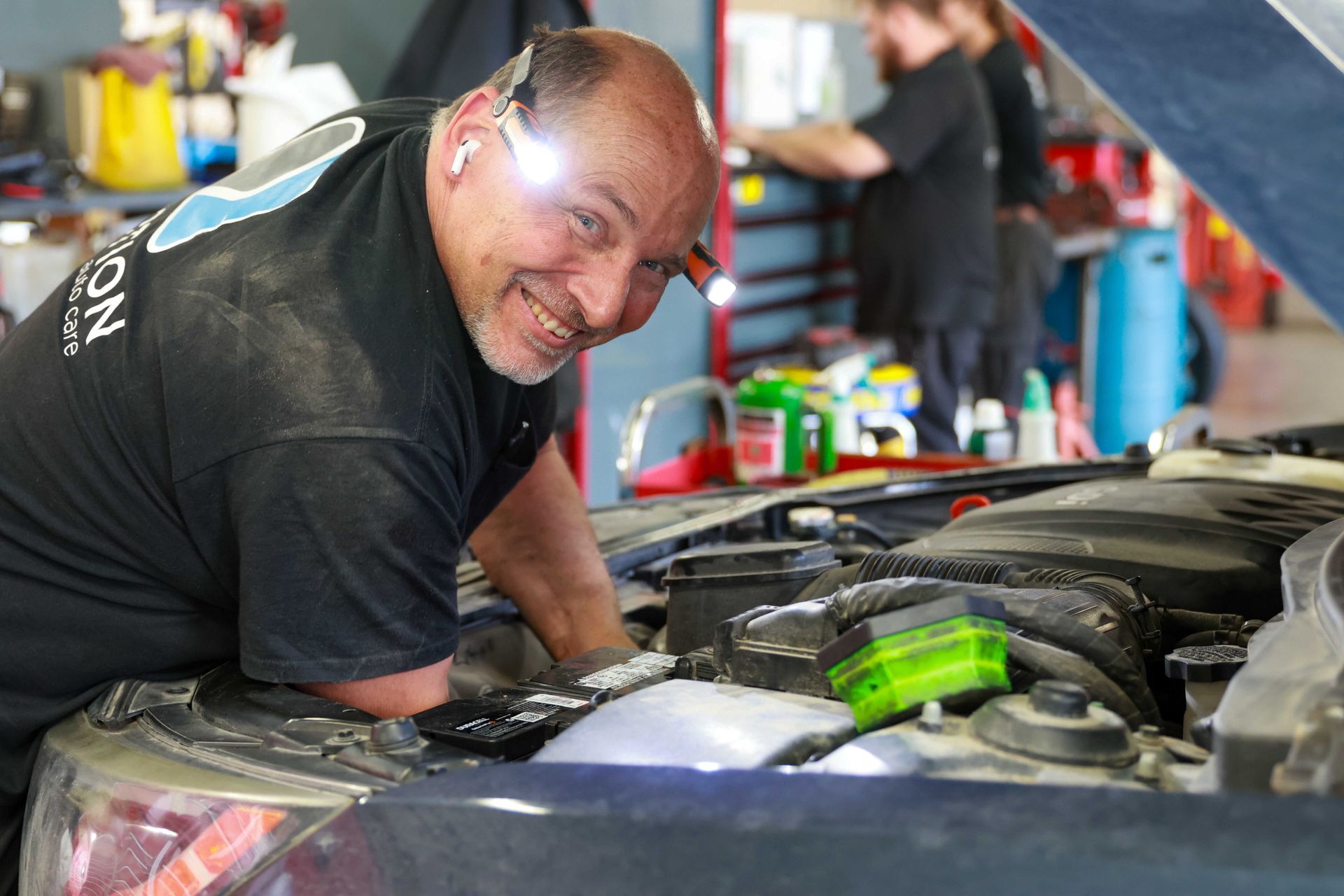 Mechanic inspecting a maroon car with open hood in an auto repair shop