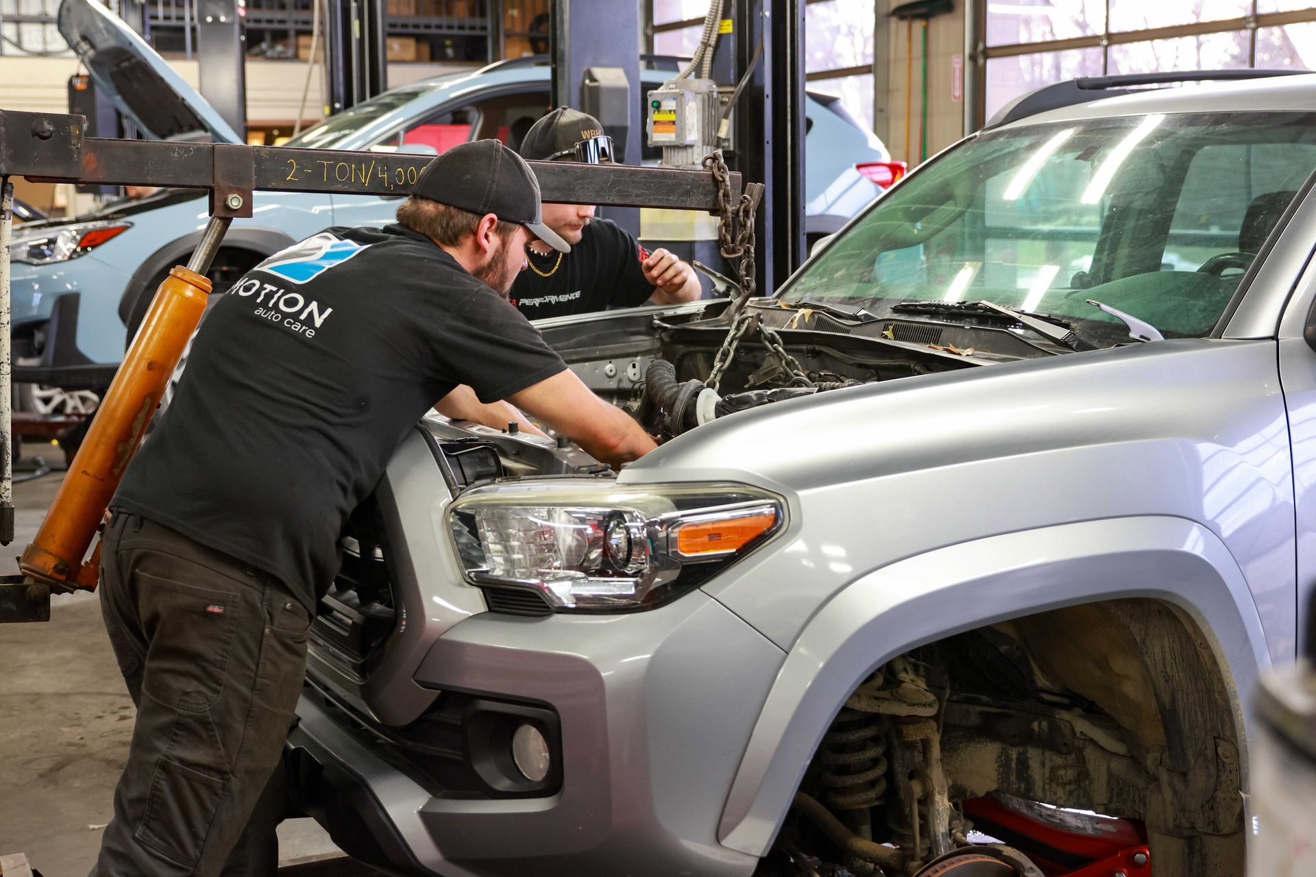 Mechanic working on the front of a silver SUV in an auto repair shop
