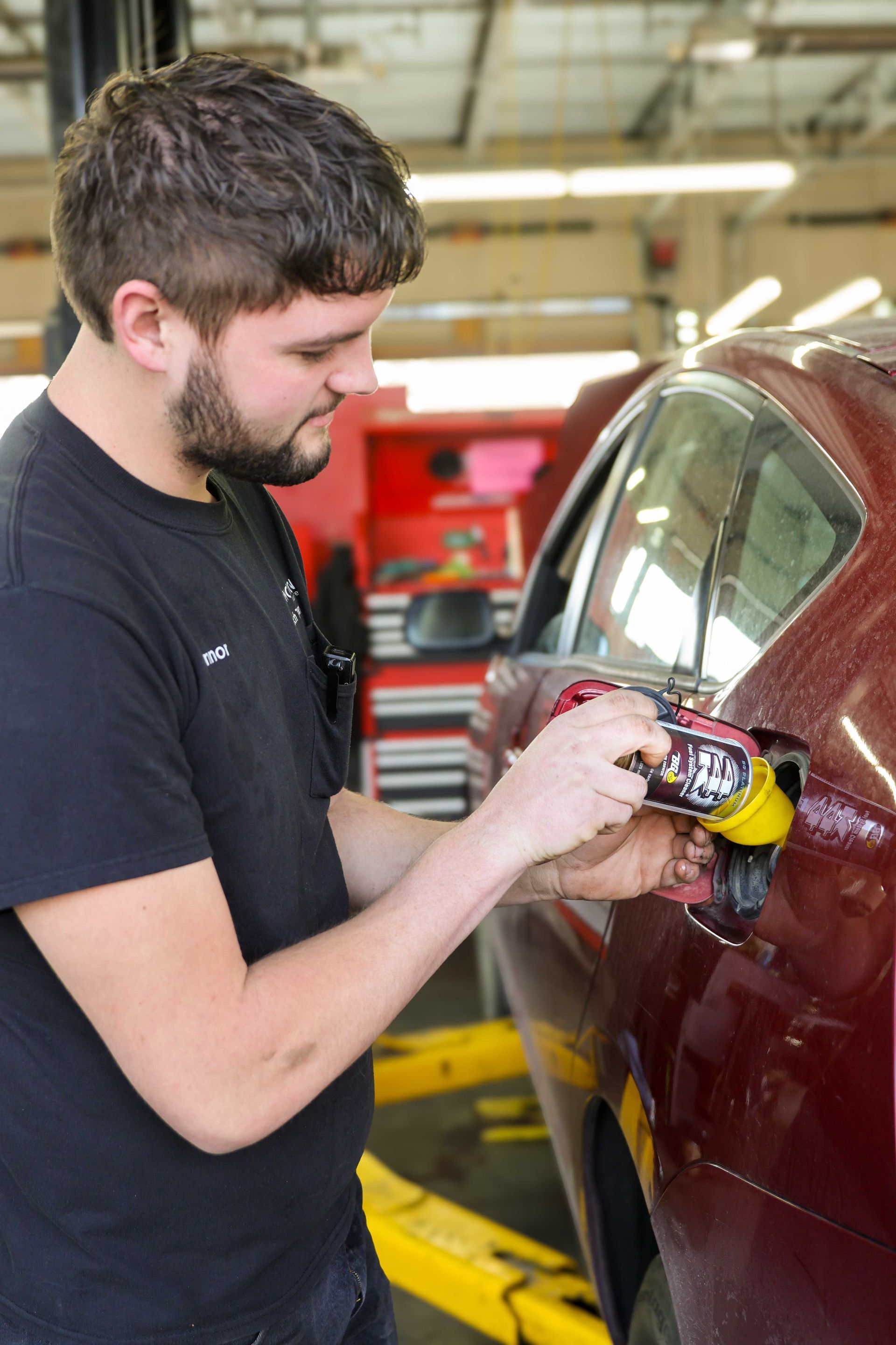Man using a handheld polisher on a red car in an auto repair shop