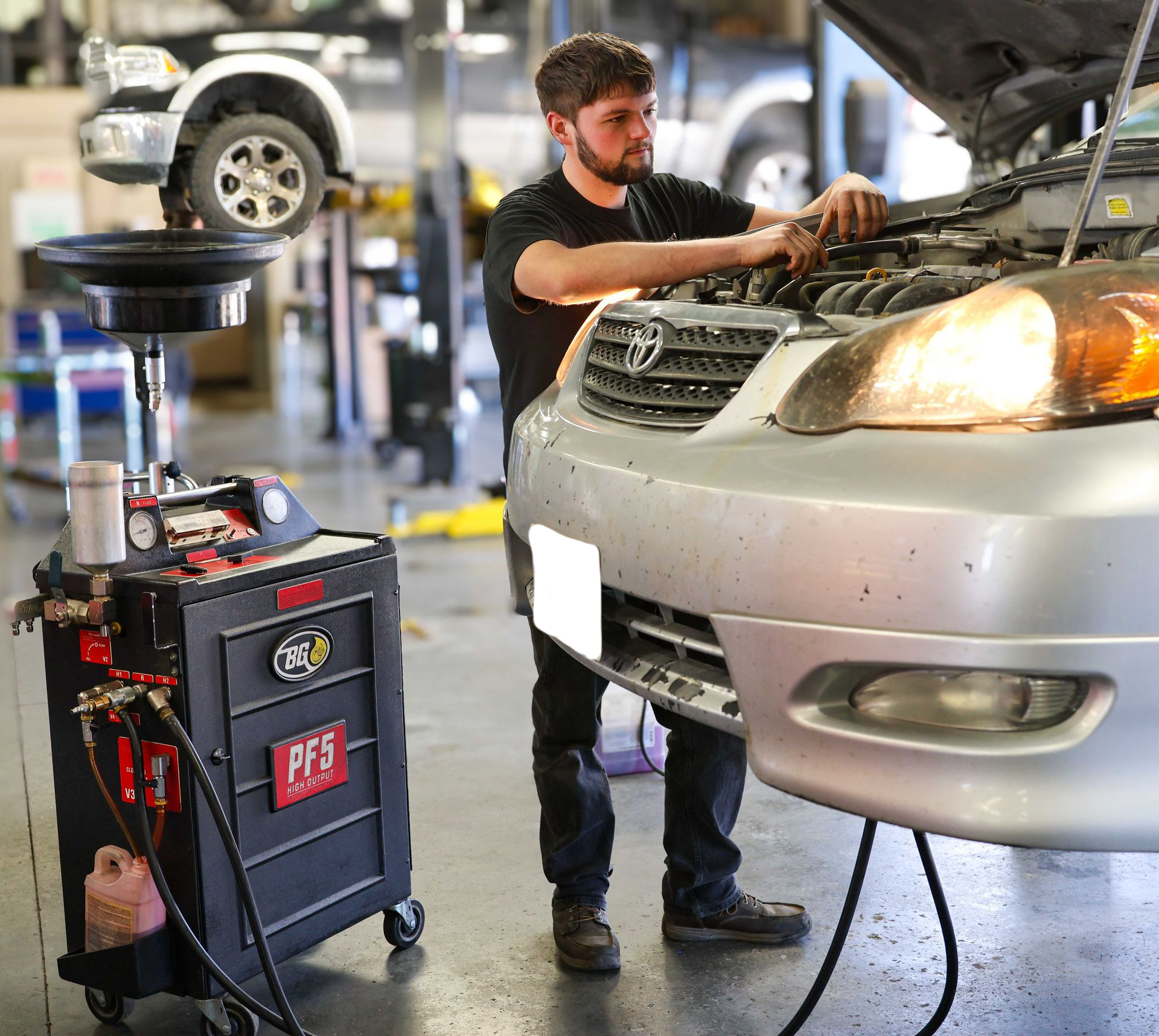 Mechanic working under a silver car in an auto repair shop beside a diagnostic machine