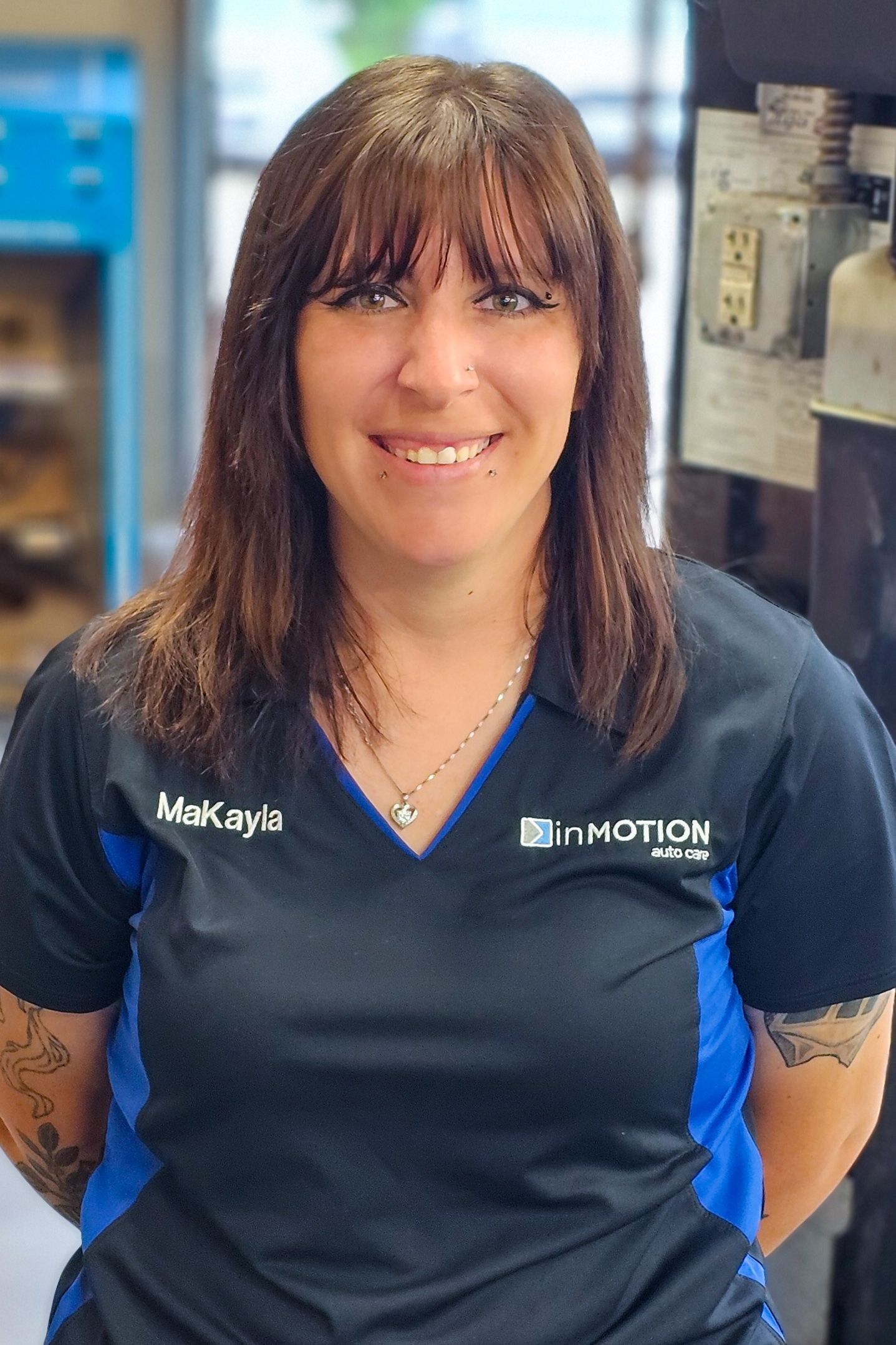 Woman in navy polo shirt smiling indoors, standing in a workplace setting.