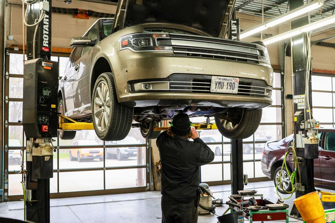Mechanic inspecting a silver SUV on a lift in an auto repair shop