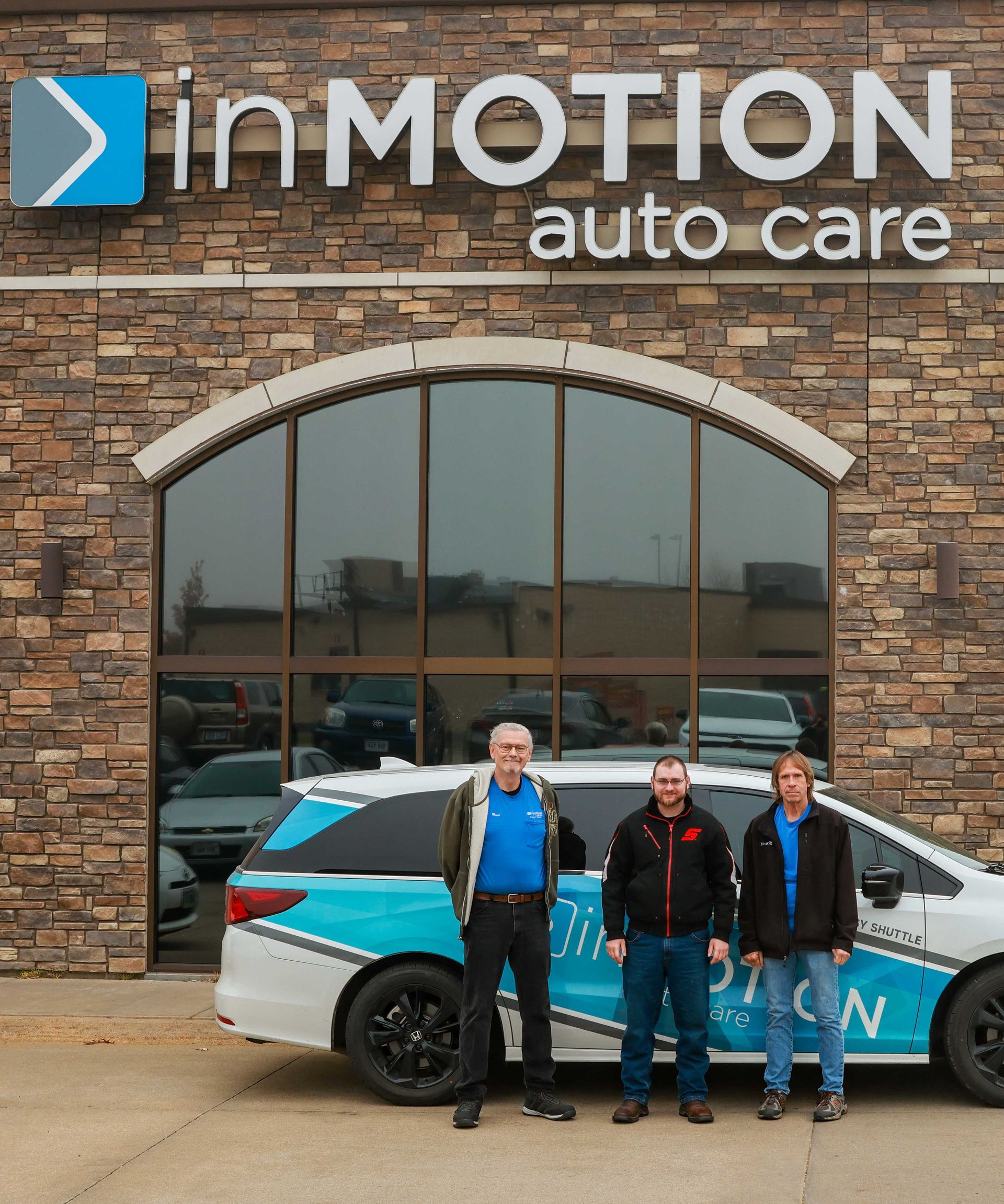 Three people standing in front of InMotion Auto Care, beside a blue-and-white car