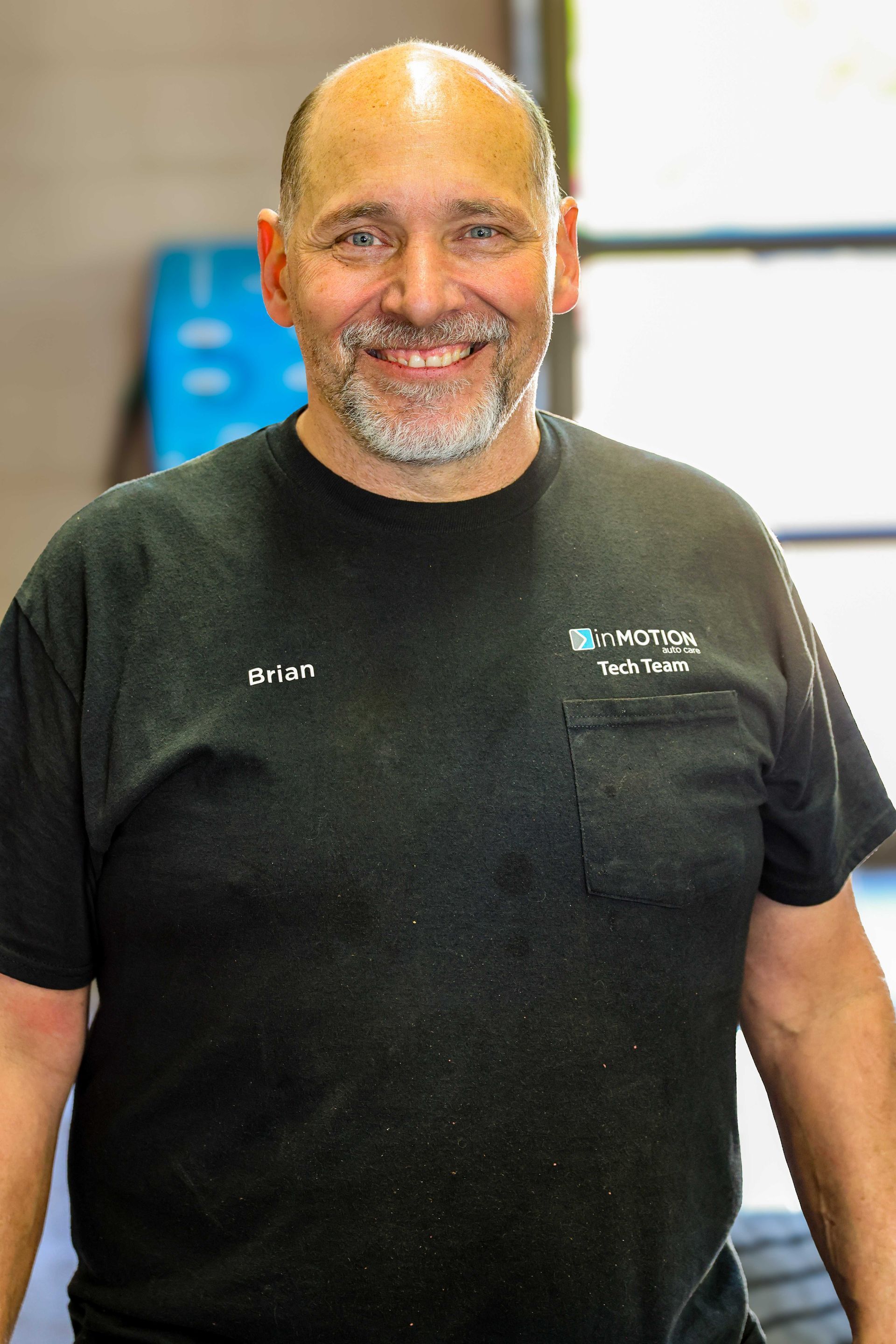 Smiling man in a black T-shirt standing indoors near a window.