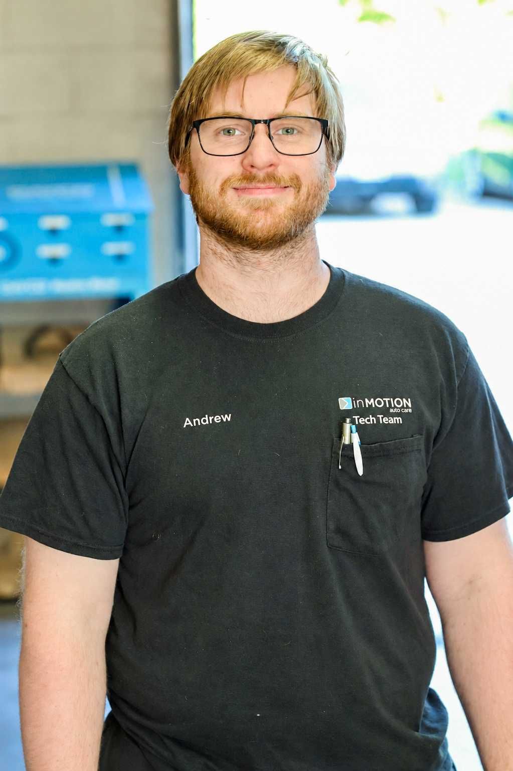 Man standing indoors in a black T-shirt and glasses, smiling softly.