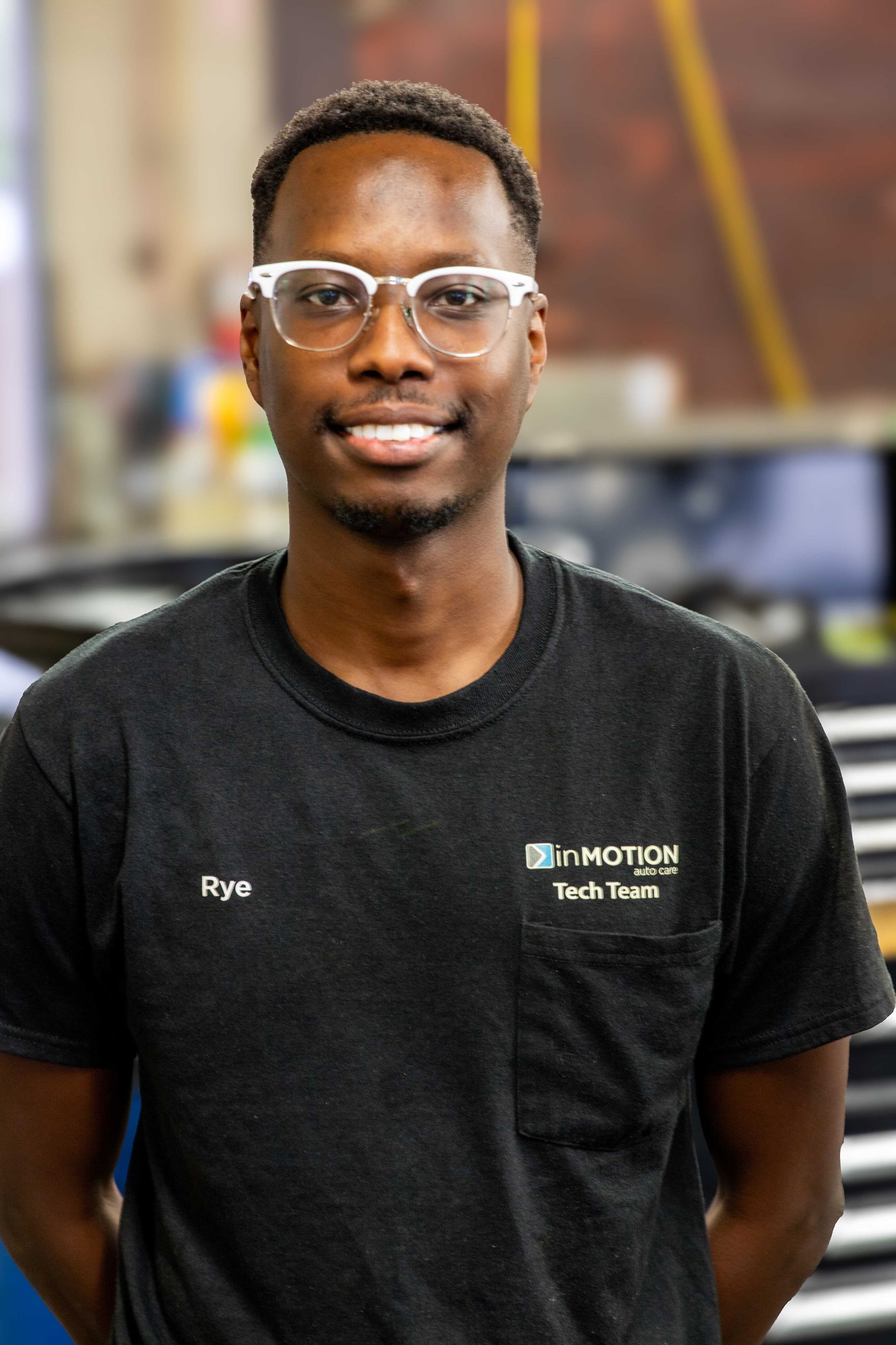 Smiling man in glasses wearing a black T-shirt with a company logo, standing indoors.