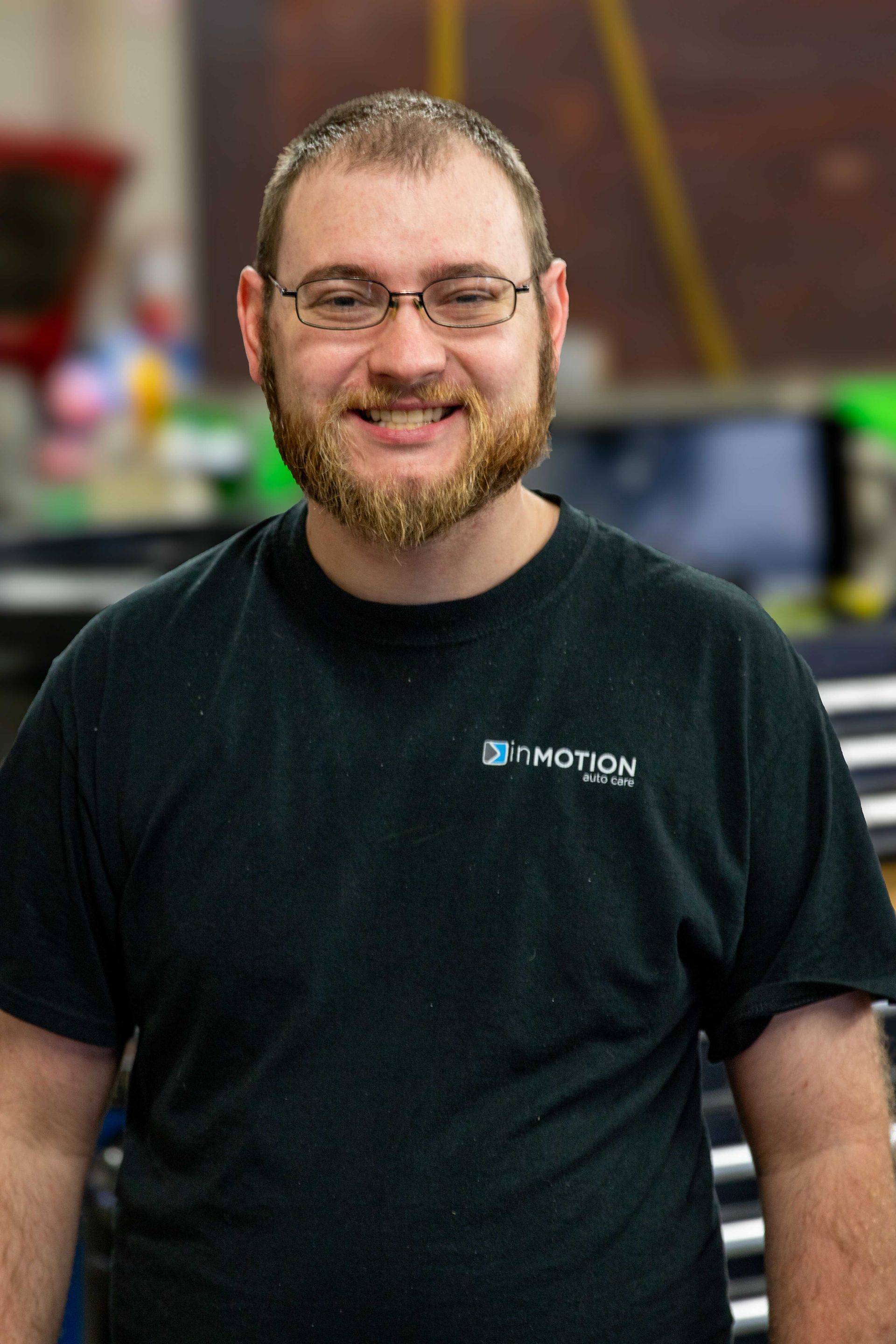 Smiling person in glasses and a black T-shirt standing indoors with a blurred background