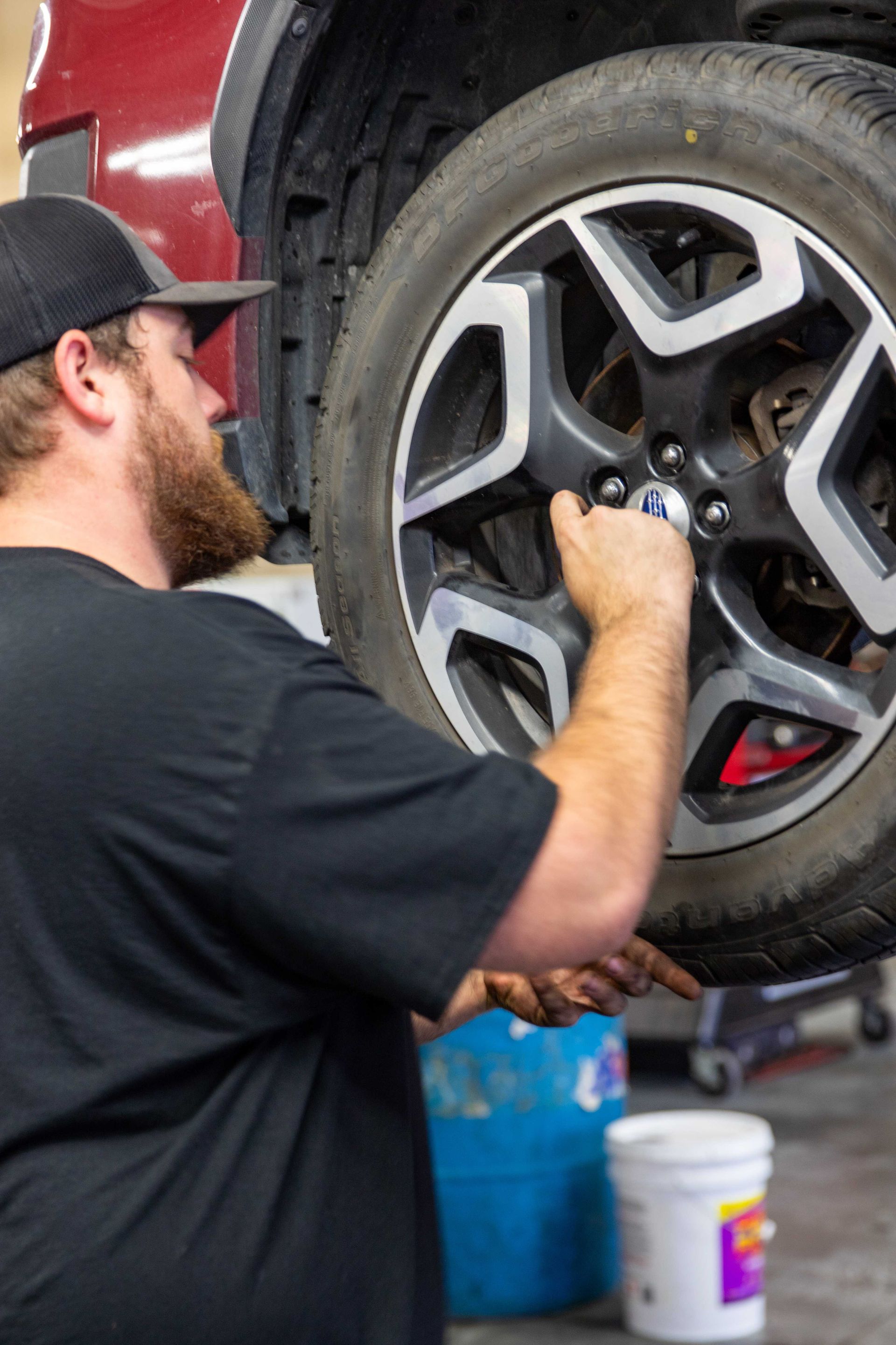 Mechanic tightening lug nuts on a red truck wheel in a garage