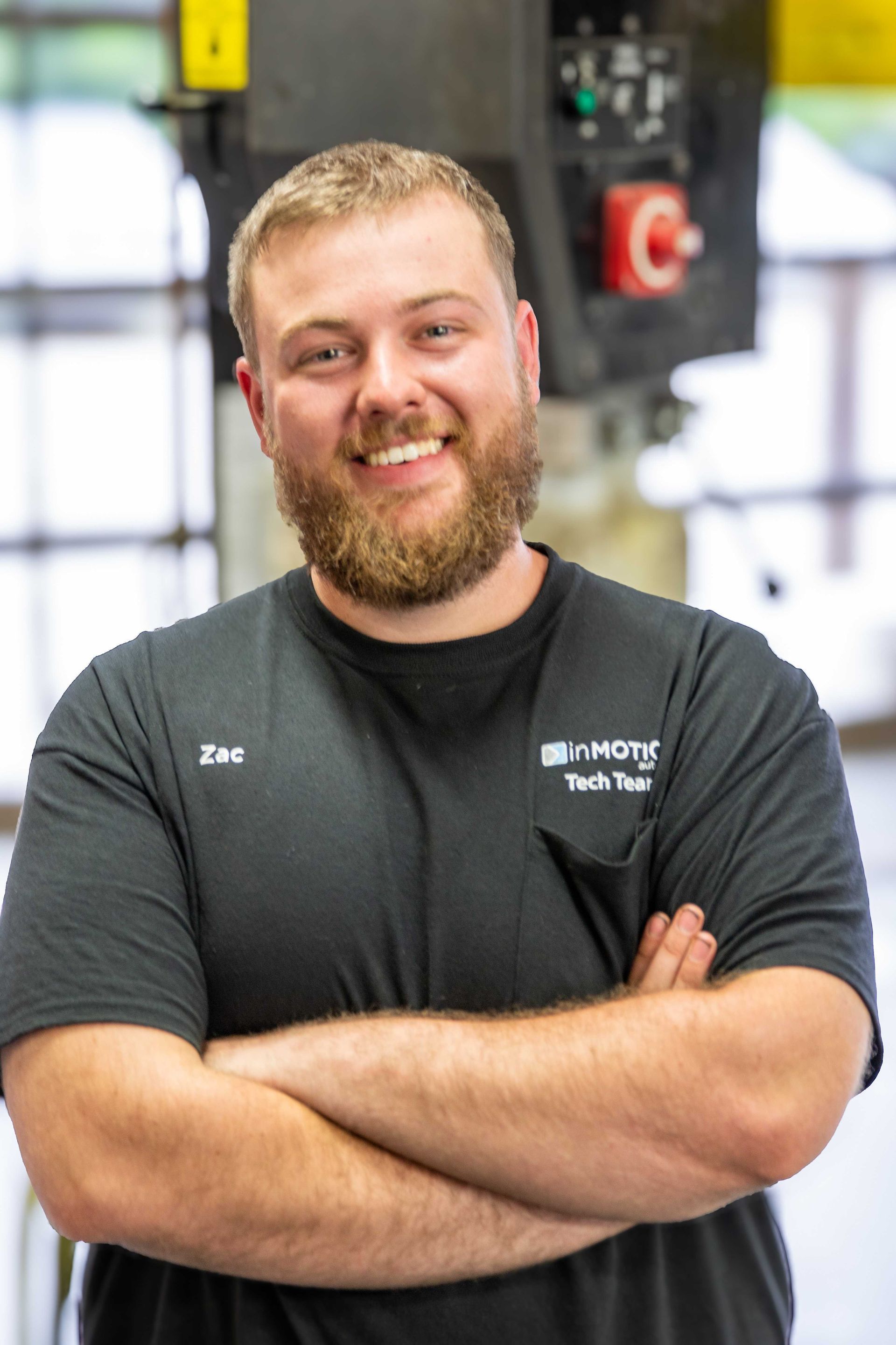 Smiling man with crossed arms in a black T-shirt standing in a gym or workshop.