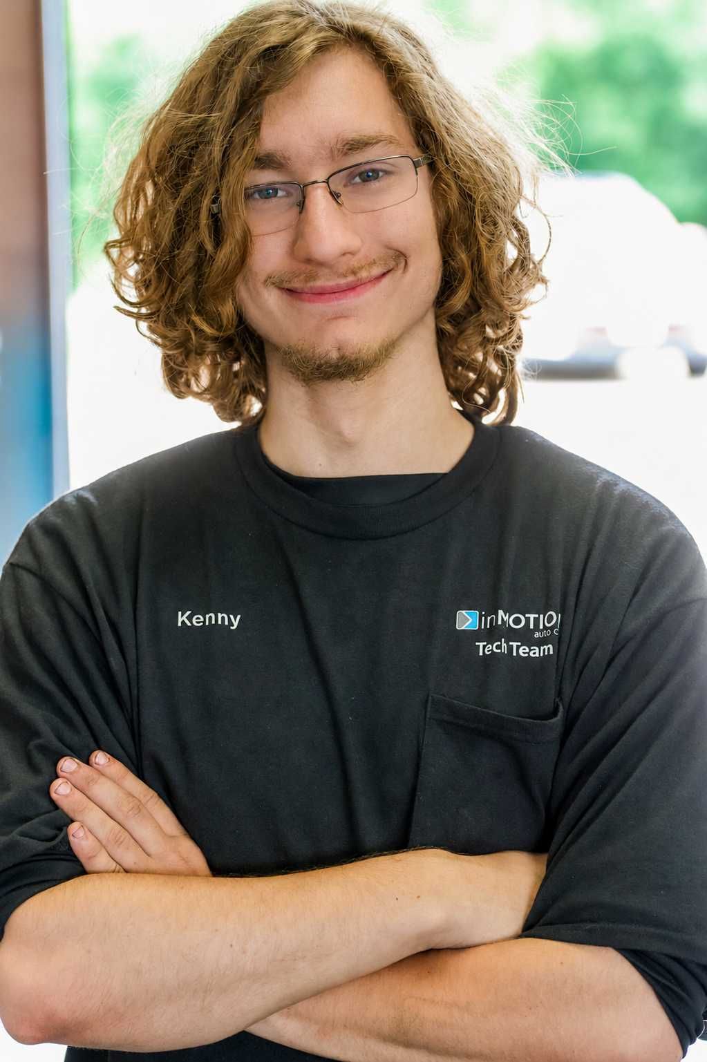 Smiling man in glasses wearing a black T-shirt with a company logo, standing indoors.