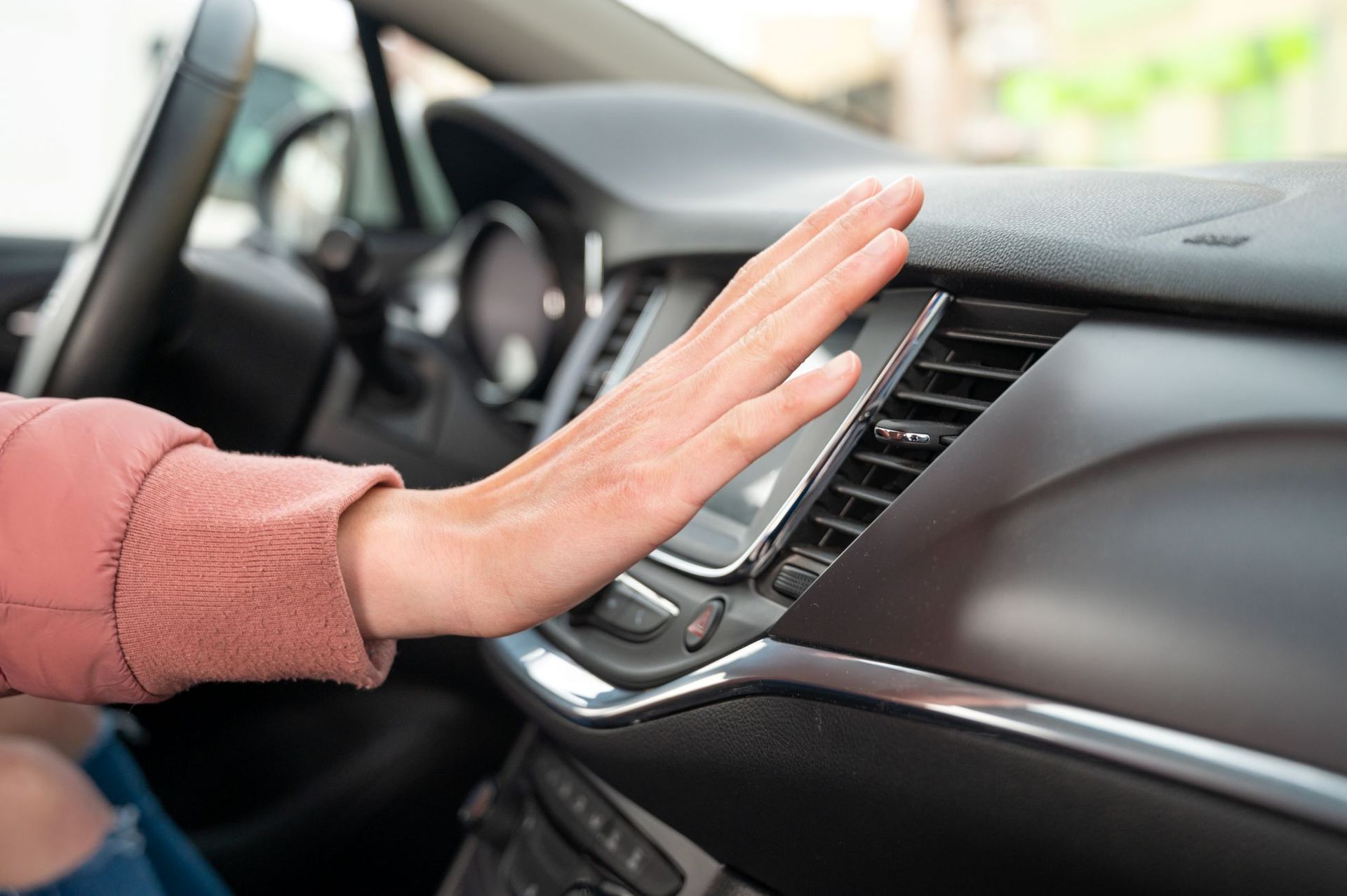 Hand reaching to tap a car dashboard touchscreen in the front seat