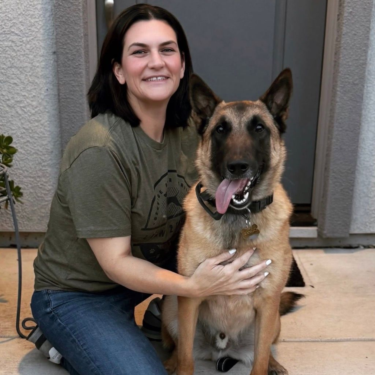 Sarah Cooper kneeling beside a German shepherd on a porch, both facing the camera and smiling.