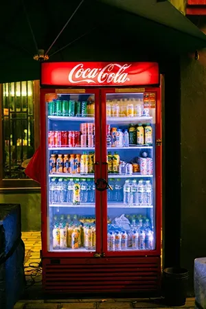 A brightly lit, red Coca-Cola vending machine filled with assorted beverages, located outdoors at night.