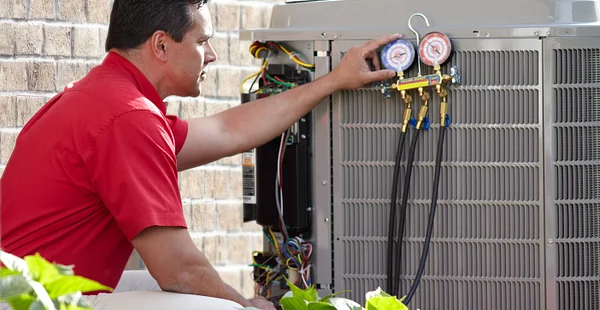 Technician in a red shirt checking the refrigerant pressure gauges on an outdoor residential air conditioning unit.