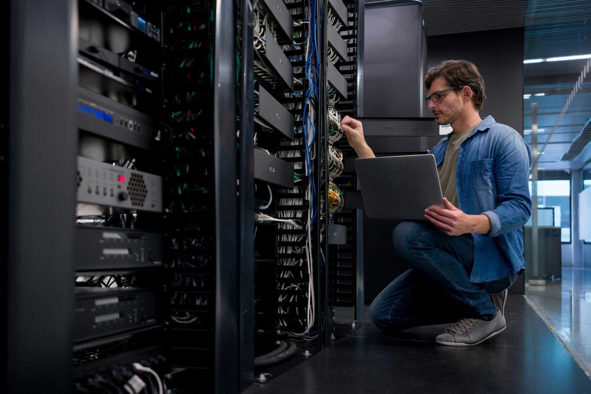 Male IT managed service provider fixing a network server at an office with laptop in hands.