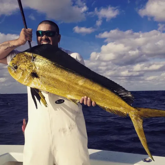 Person on a boat holding a large yellow mahi-mahi fish against a blue ocean and cloudy sky