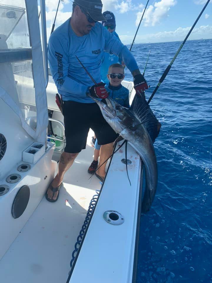Two anglers on a boat hold a long silver fish over blue ocean water.