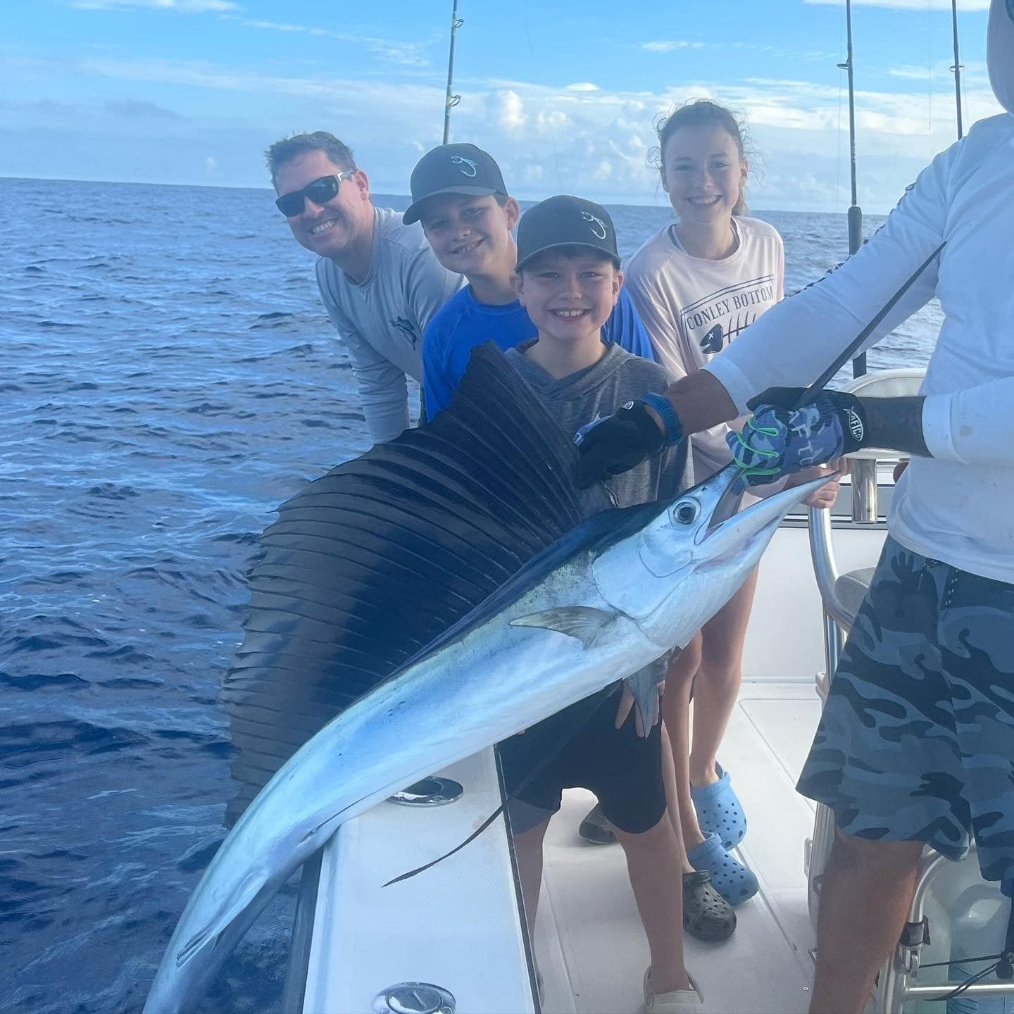 Four people on a boat proudly holding a large fish on open water.