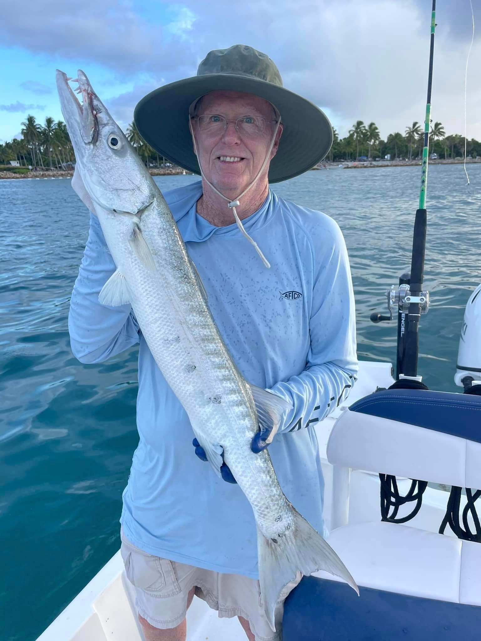 Angler on a boat holding a large silver fish over blue water under a sunny sky