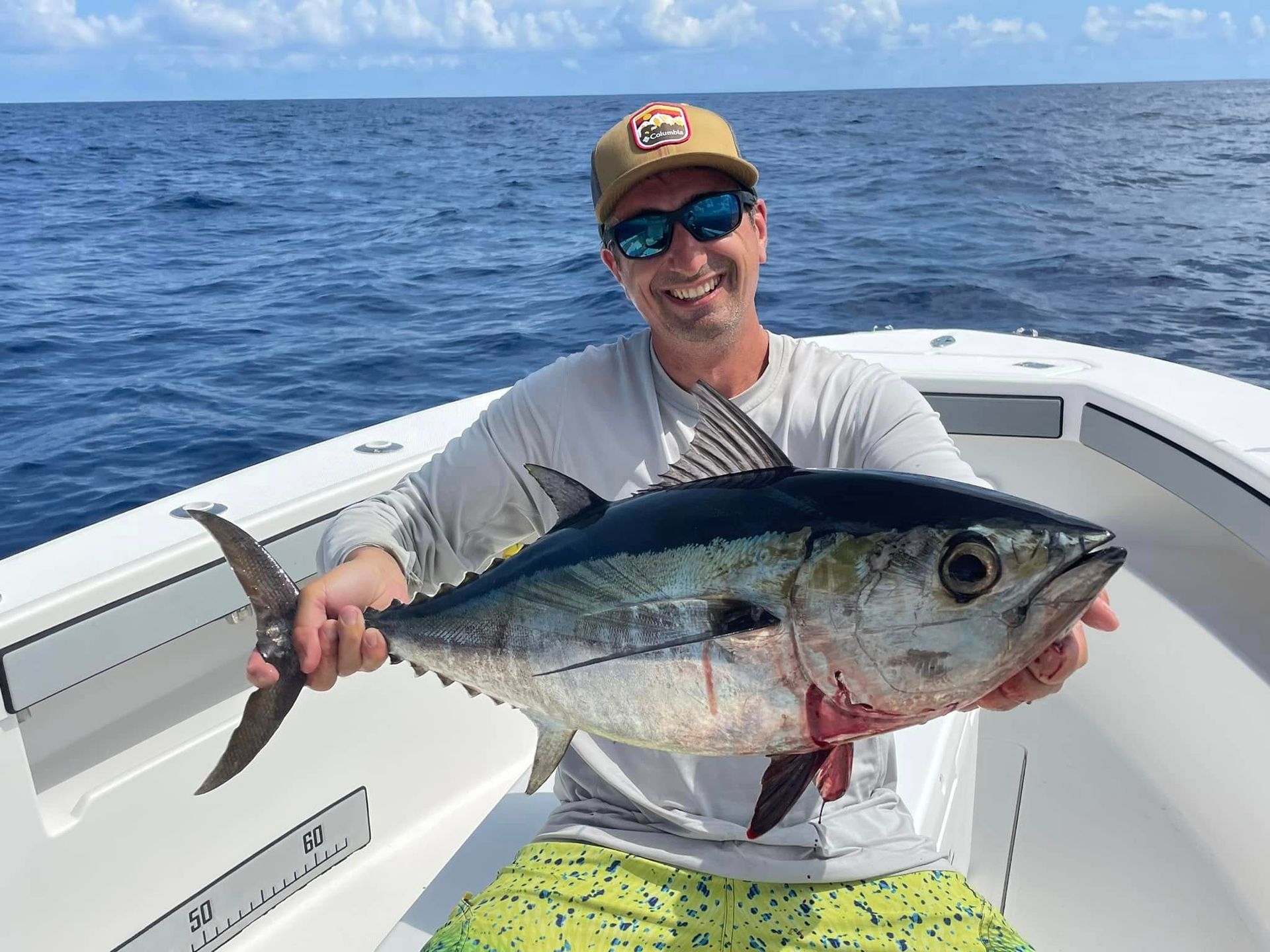 Smiling angler on a boat holding a large tuna over the ocean