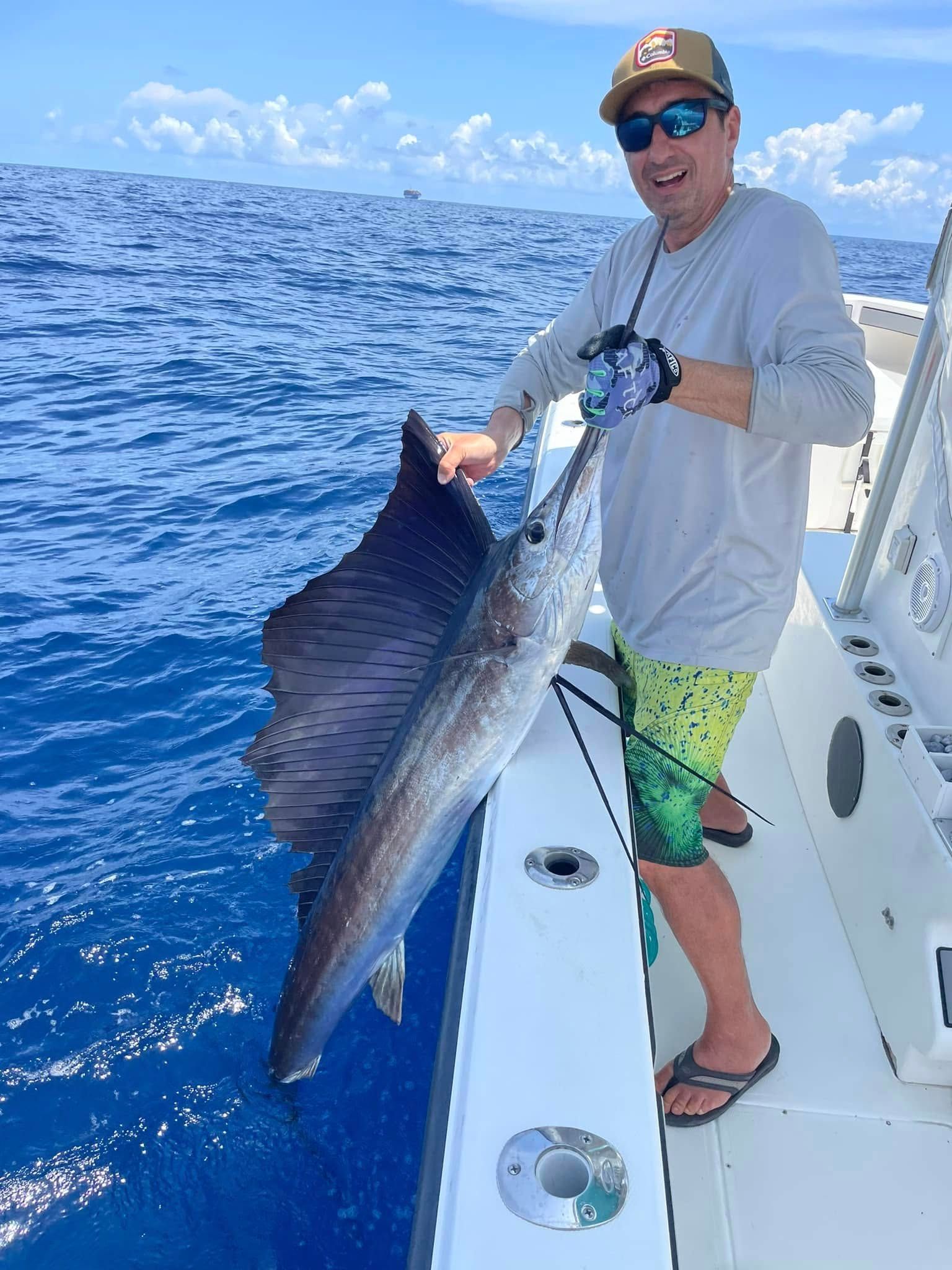 Man on a boat holding a large sailfish beside bright blue ocean water