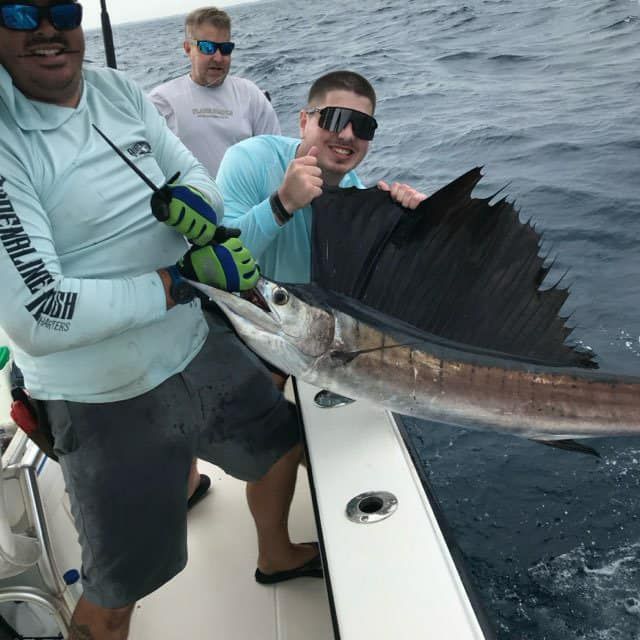 Two anglers on a boat hold a large swordfish beside the rail on choppy water.