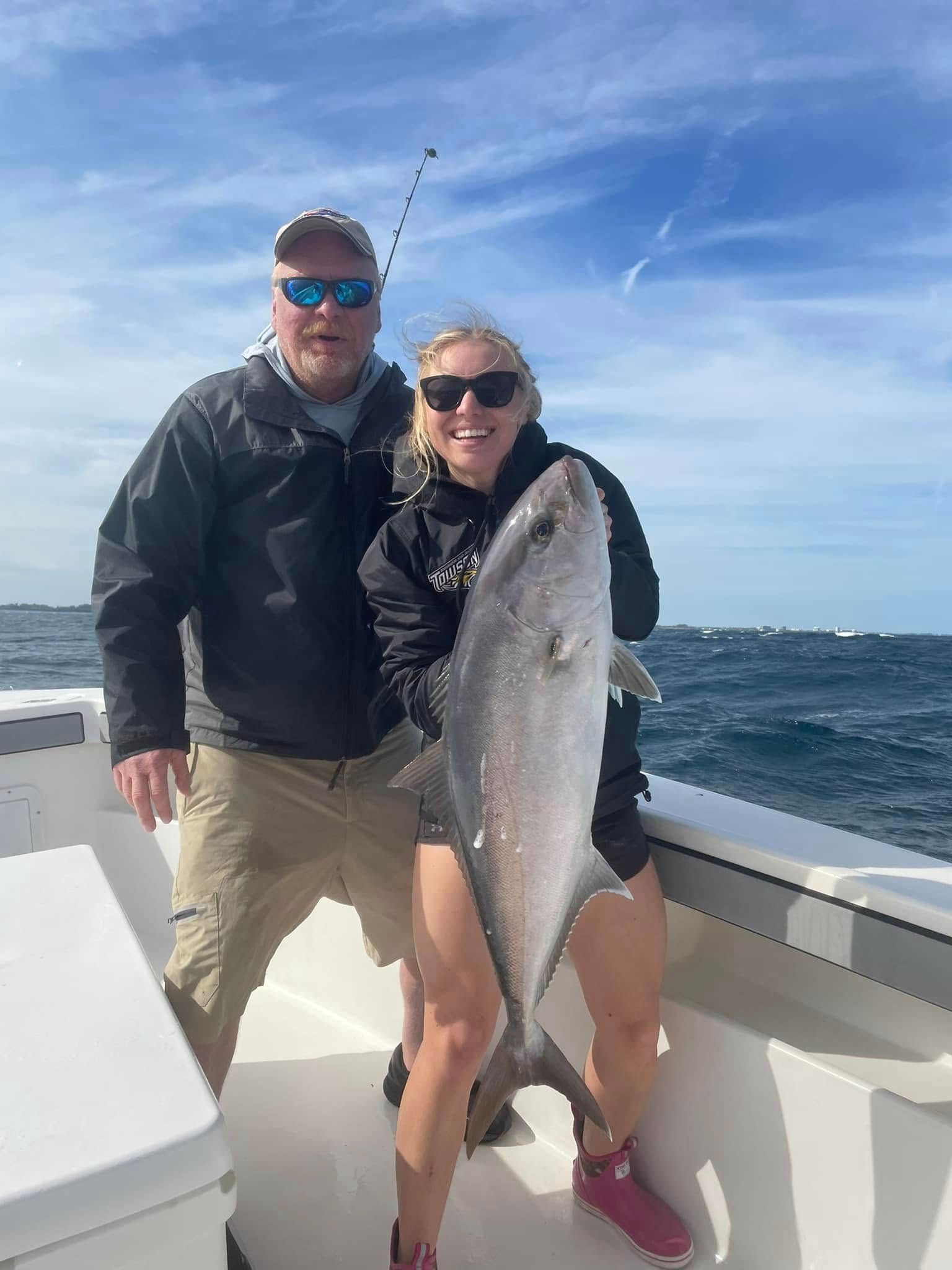 Two people on a boat holding a large silver fish, with ocean and blue sky in the background
