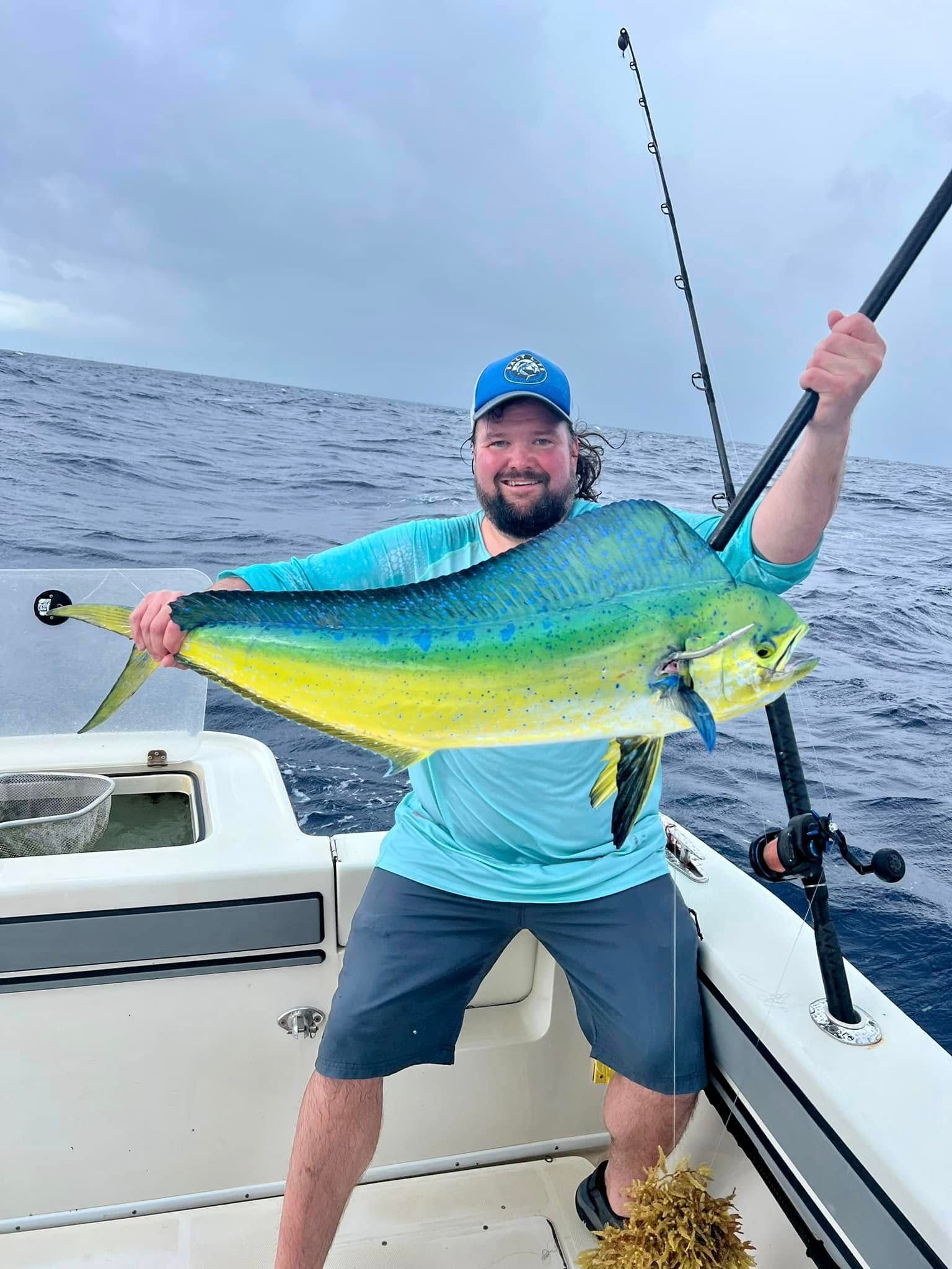 Angler on a boat proudly holds a large yellow-green fish with the ocean in the background
