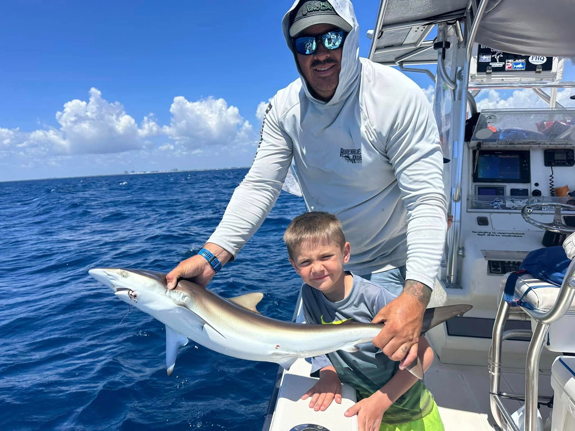 Man and boy on a boat holding a large fish on the open ocean under a blue sky
