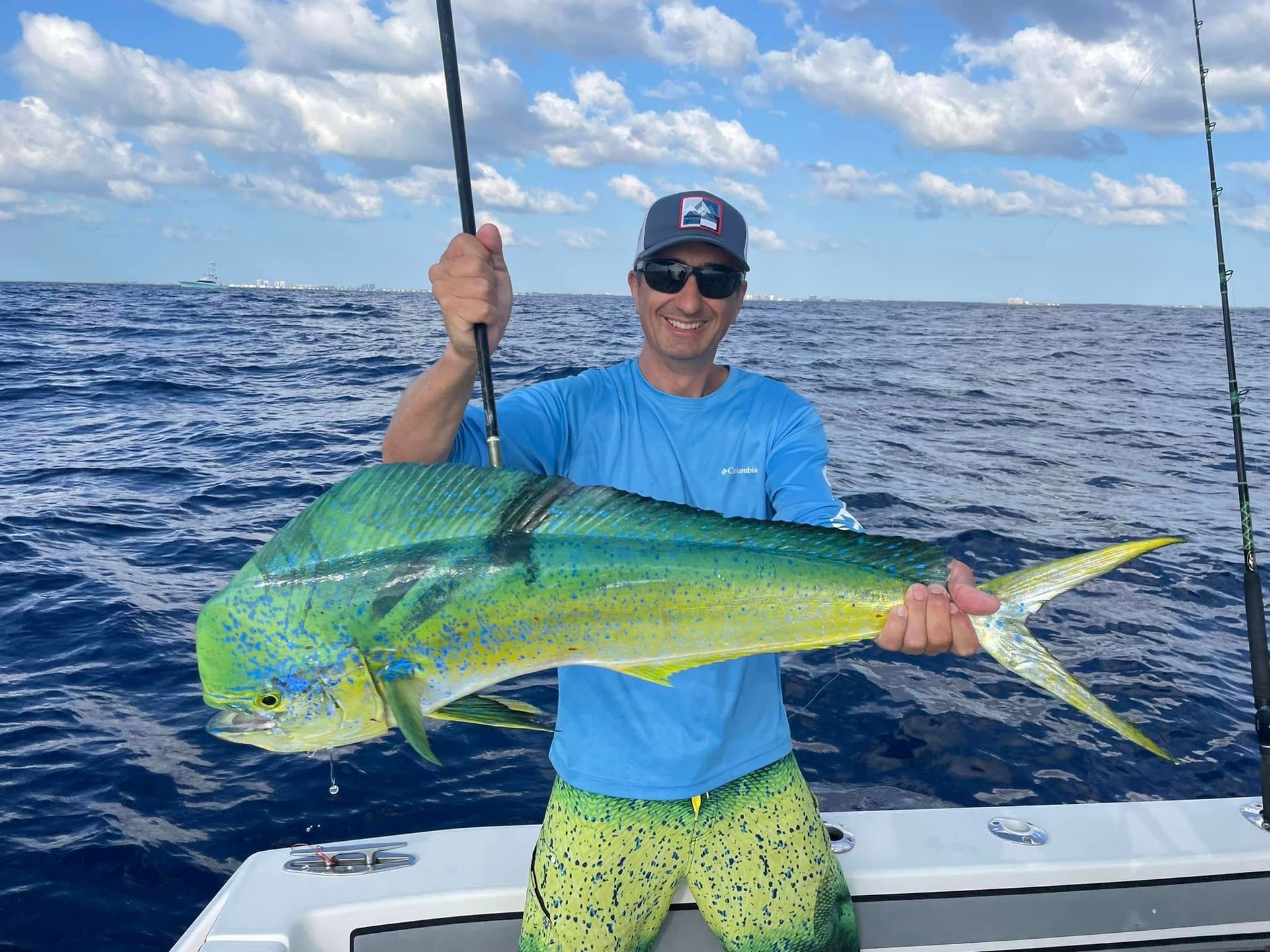 Person on a boat holding a large green-yellow fish against the ocean and cloudy sky.