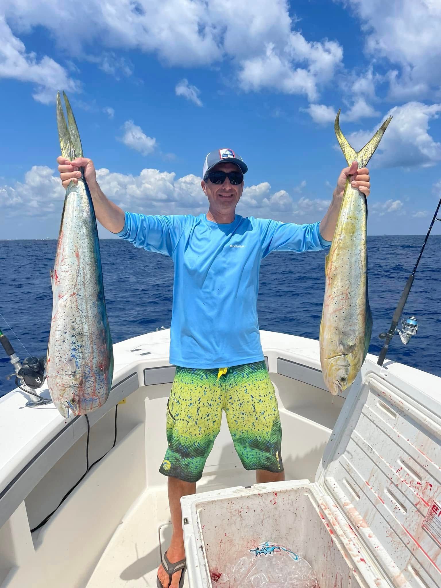 Angler on a boat holding two large fish, with ocean and blue sky in the background.