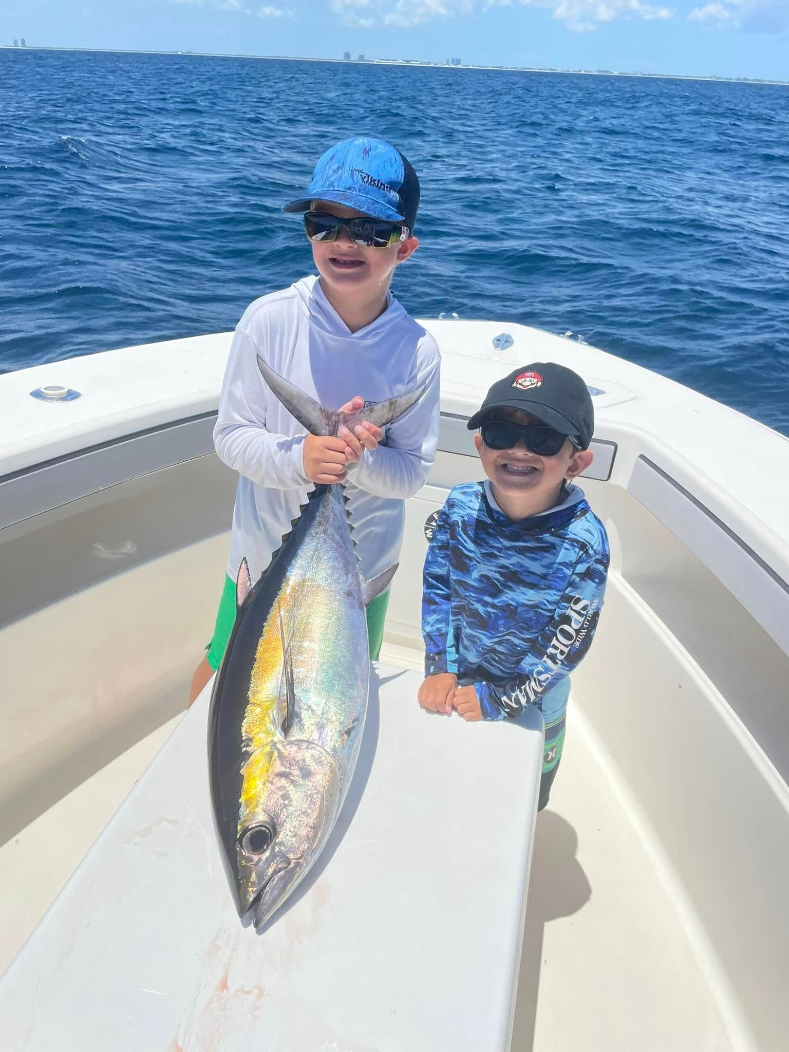Two children on a boat hold a large fish on a sunny ocean trip.