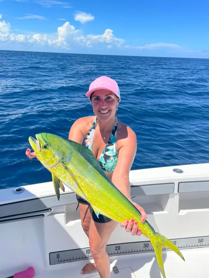 Person on a boat holding a large yellow fish on a sunny ocean.